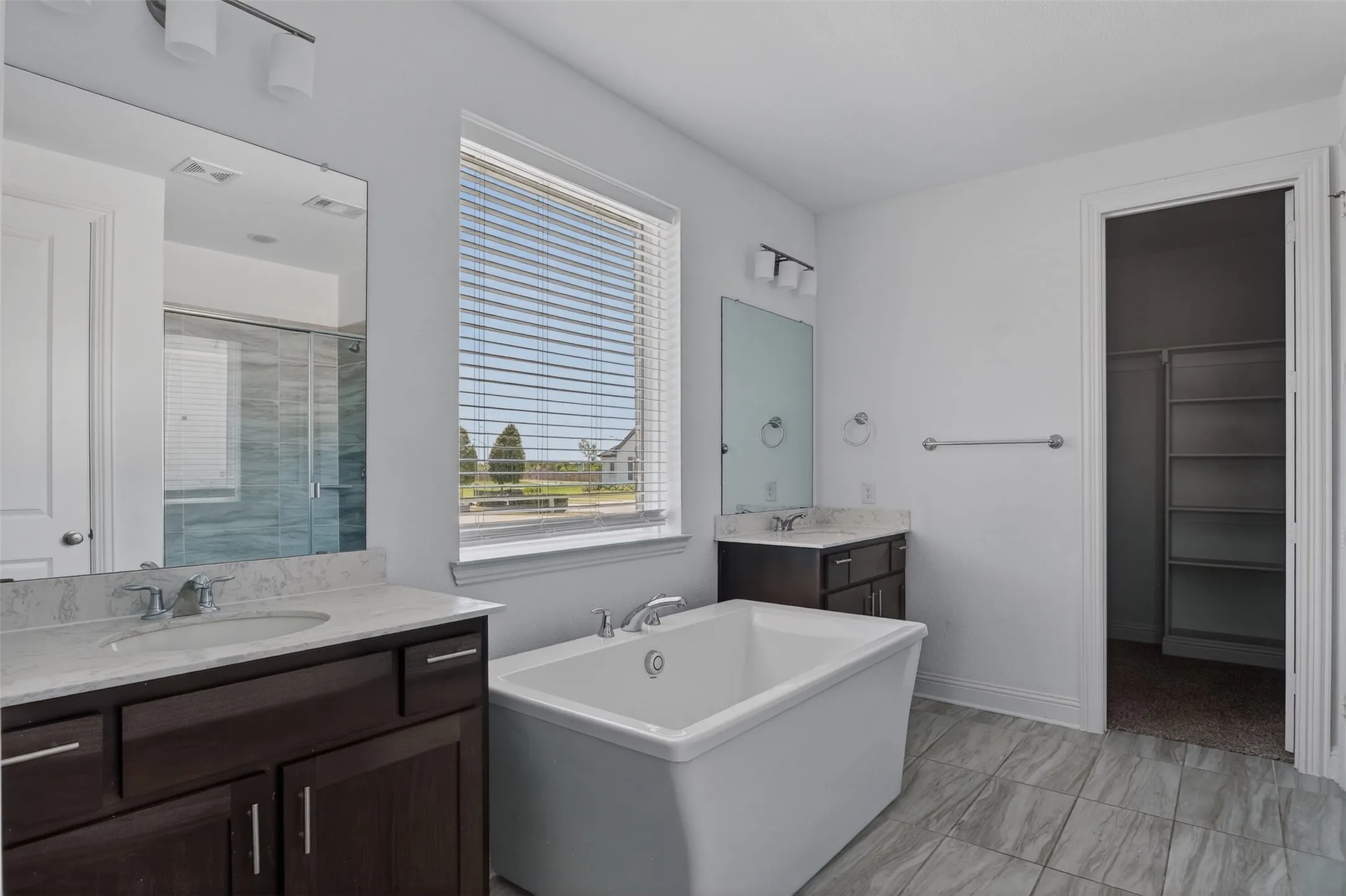 Spacious bathroom featuring a freestanding tub, dual vanity with undermount sinks, separate glass-enclosed shower, and tile flooring