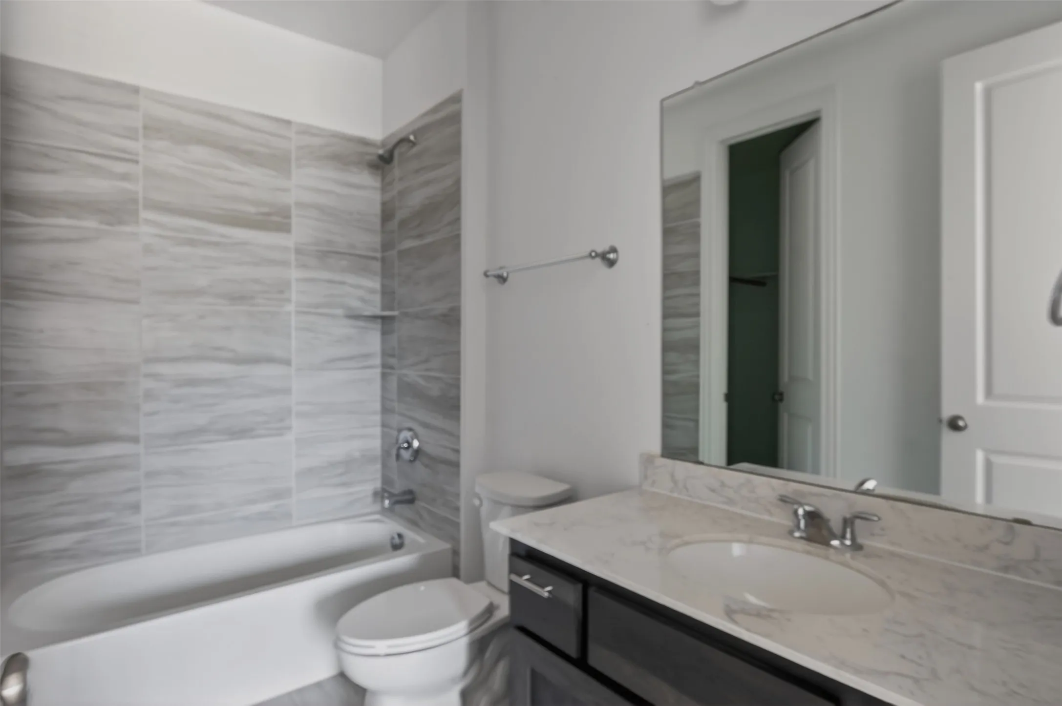 Bathroom featuring a white porcelain tub with a tiled surround, a built-in shower niche, a dark wood-finish vanity with a light stone countertop, and a chrome faucet