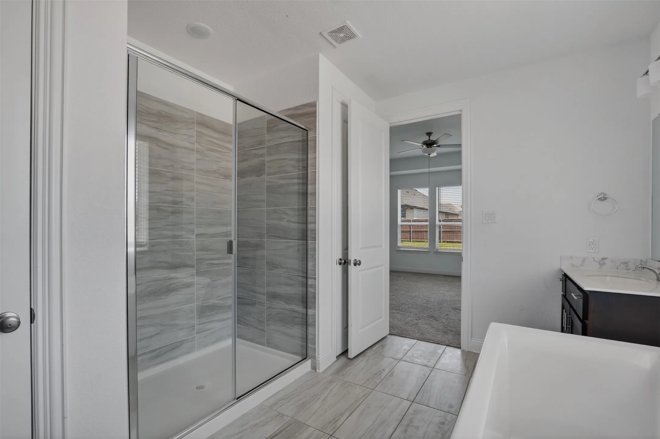 Bathroom featuring a glass-enclosed shower with gray tiled walls, a separate soaking tub, and a vanity with a white countertop