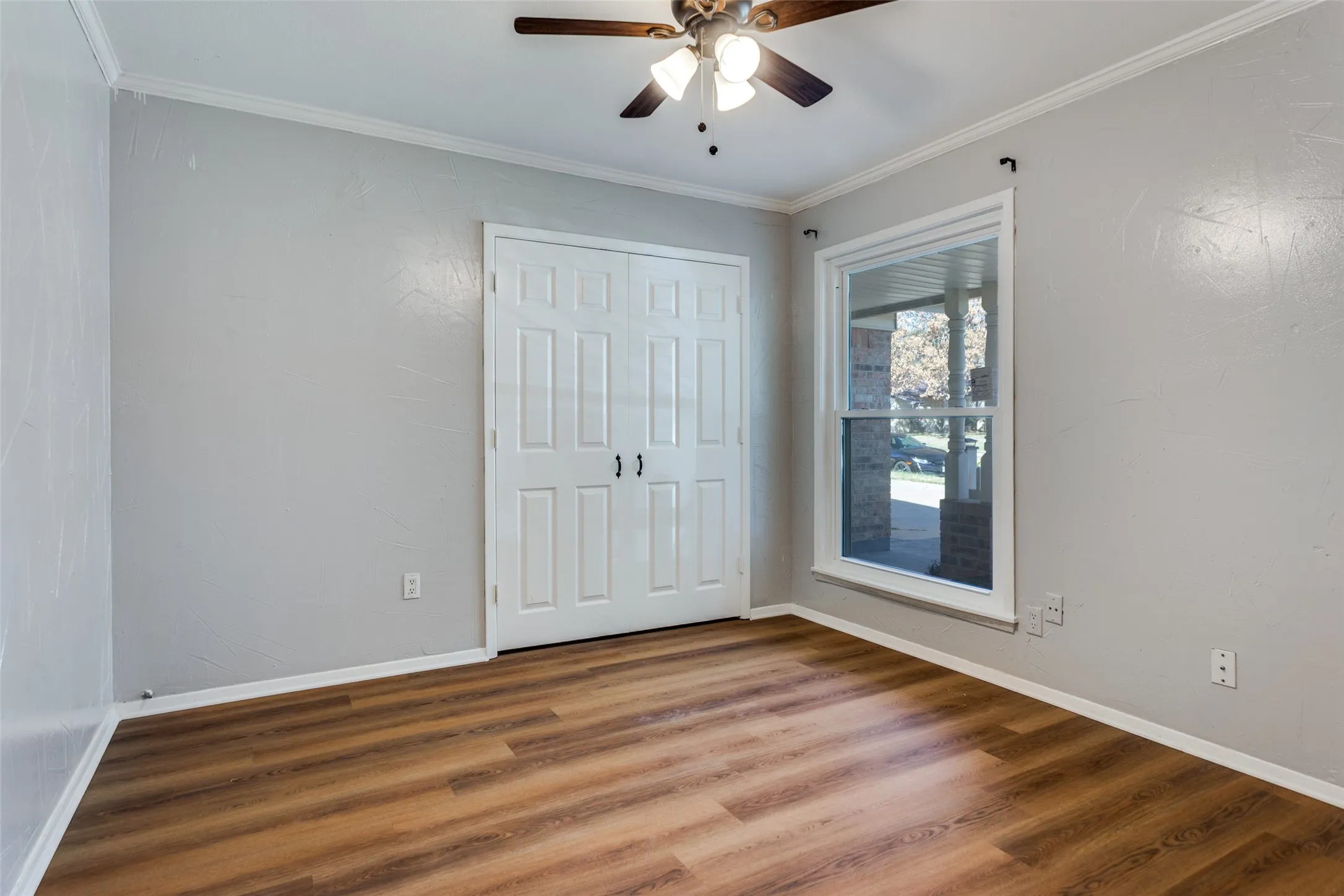 Room featuring wood-finish flooring, light gray walls, a ceiling fan with integrated lighting, and white trim