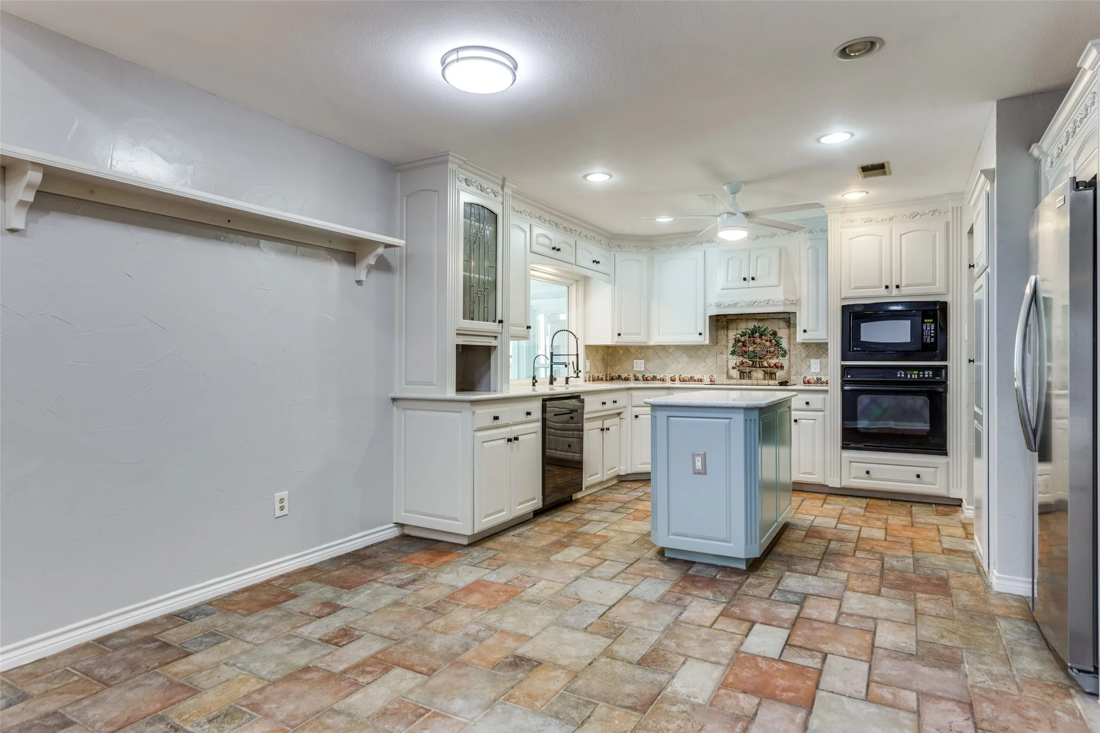 Kitchen featuring white cabinetry, built-in appliances, a light blue island with a contrasting countertop, a patterned tile backsplash, and multi-toned tile flooring
