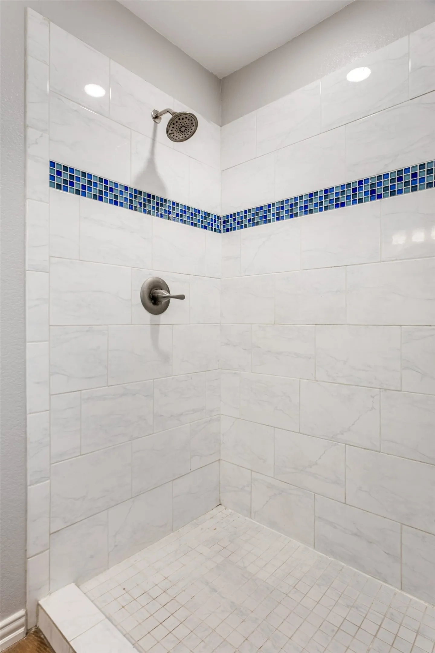 Walk-in shower featuring white subway tile walls with a blue mosaic tile accent band