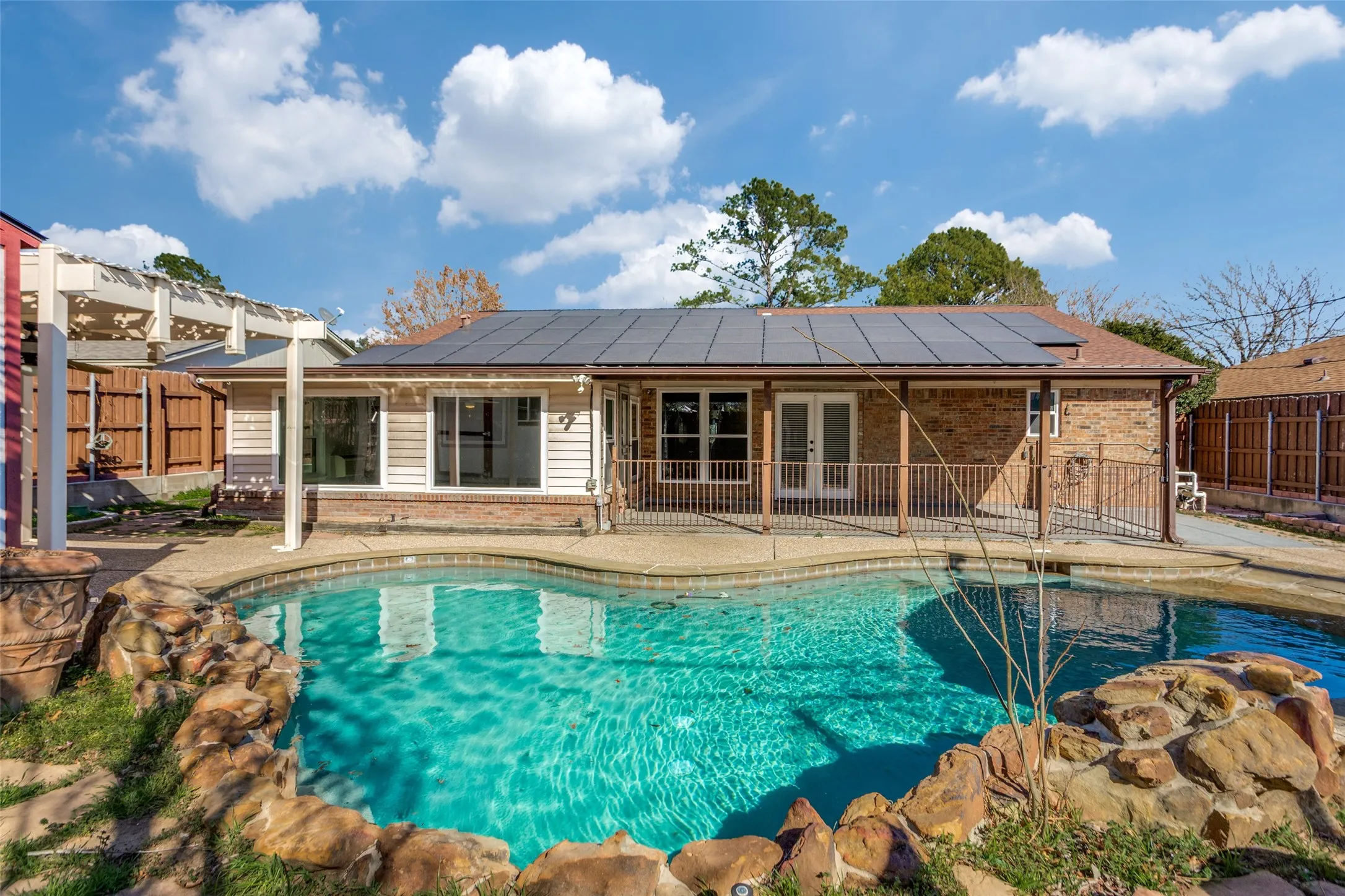 Curved backyard swimming pool with rock detailing and surrounding patio