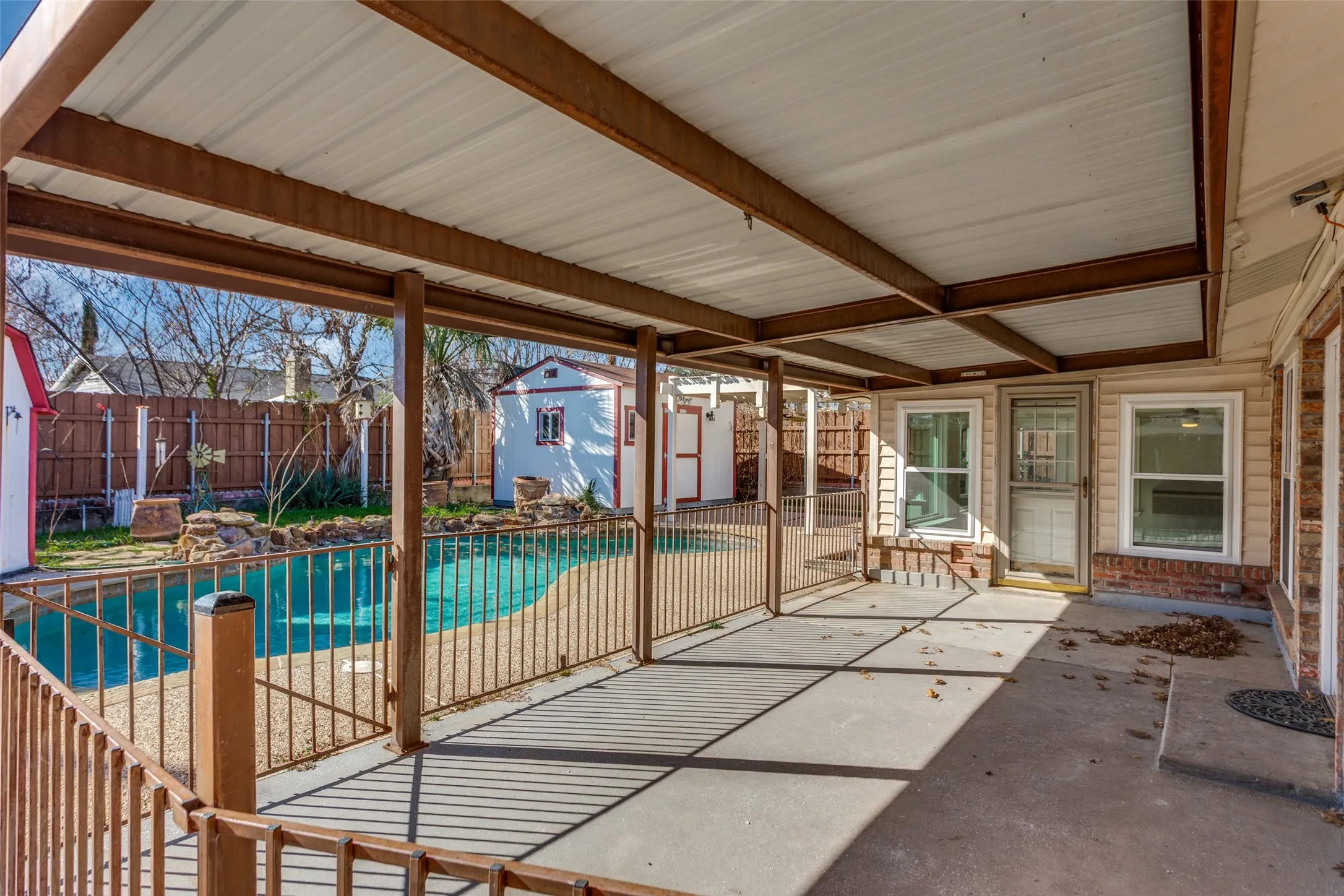 Covered patio overlooking a fenced swimming pool with a rock water feature