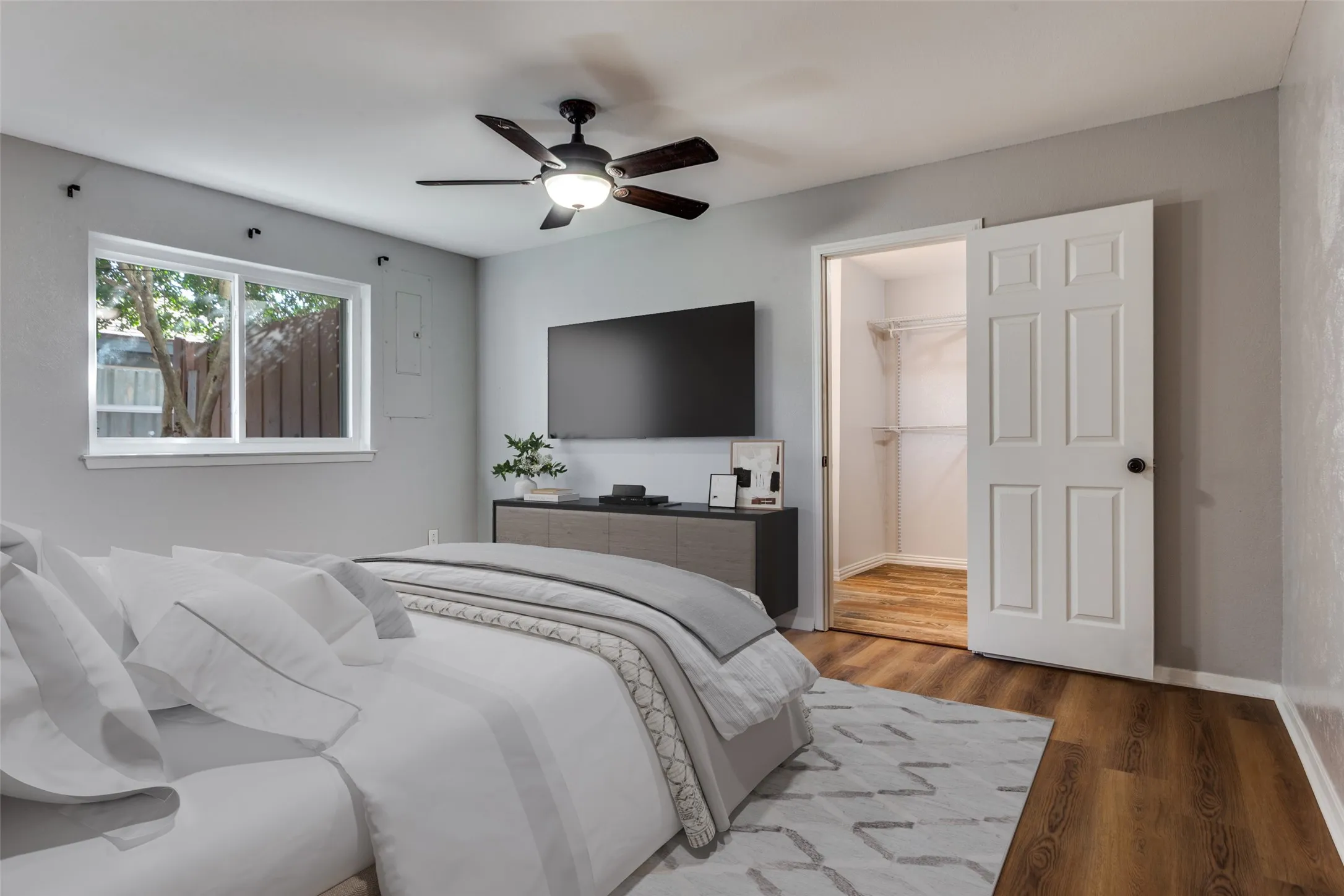 Spacious room featuring wood-finish flooring, a contemporary ceiling fan with integrated lighting, a built-in closet with shelving, and a dual-pane window (virtual staging)
