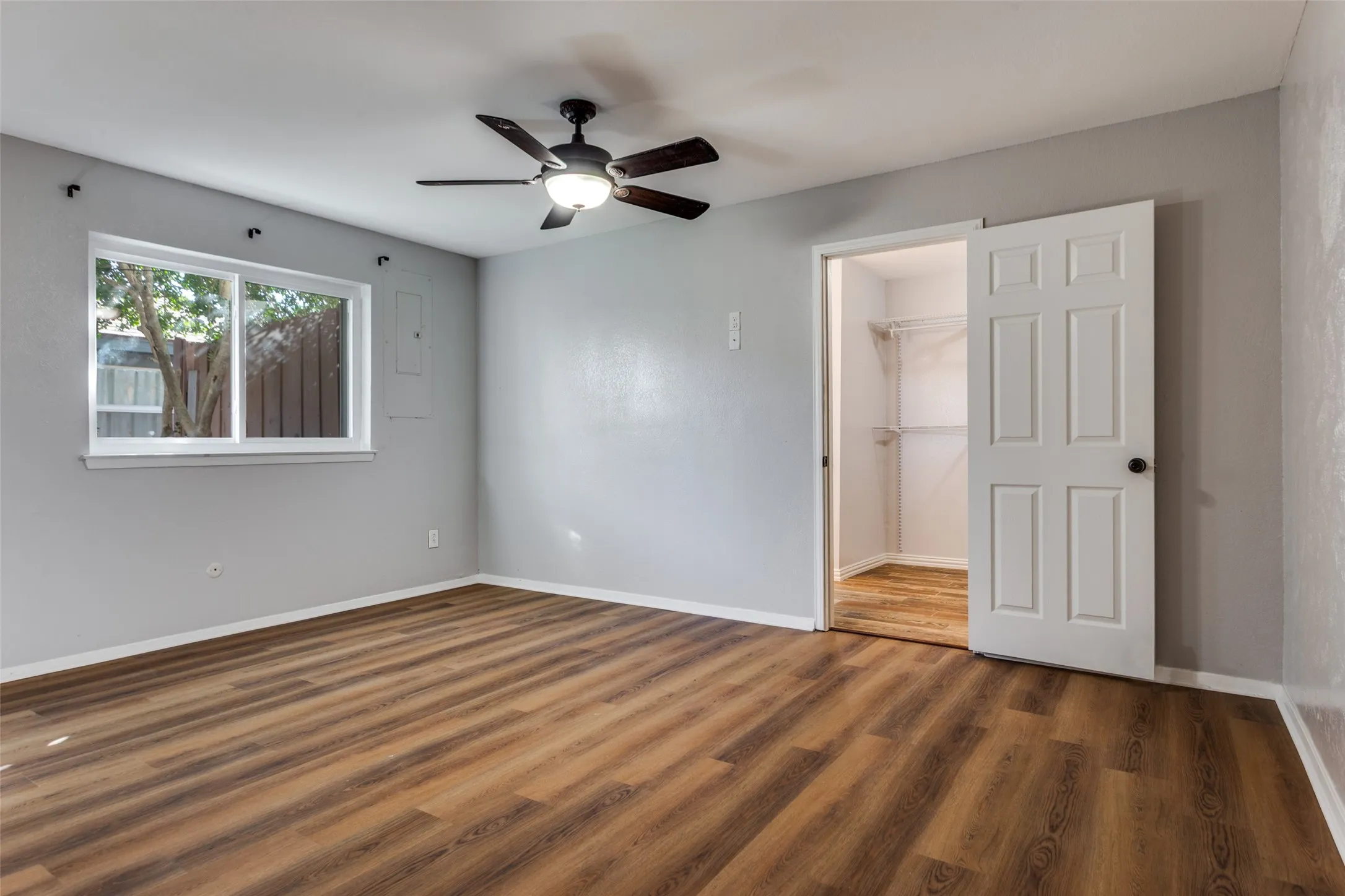 Spacious room featuring wood-finish flooring, a contemporary ceiling fan with integrated lighting, and a white-framed window