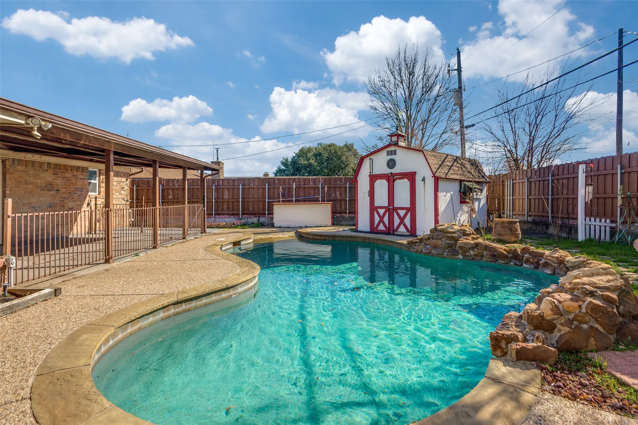 Backyard oasis featuring a freeform swimming pool with rock detailing, a covered patio, and an accessory storage building
