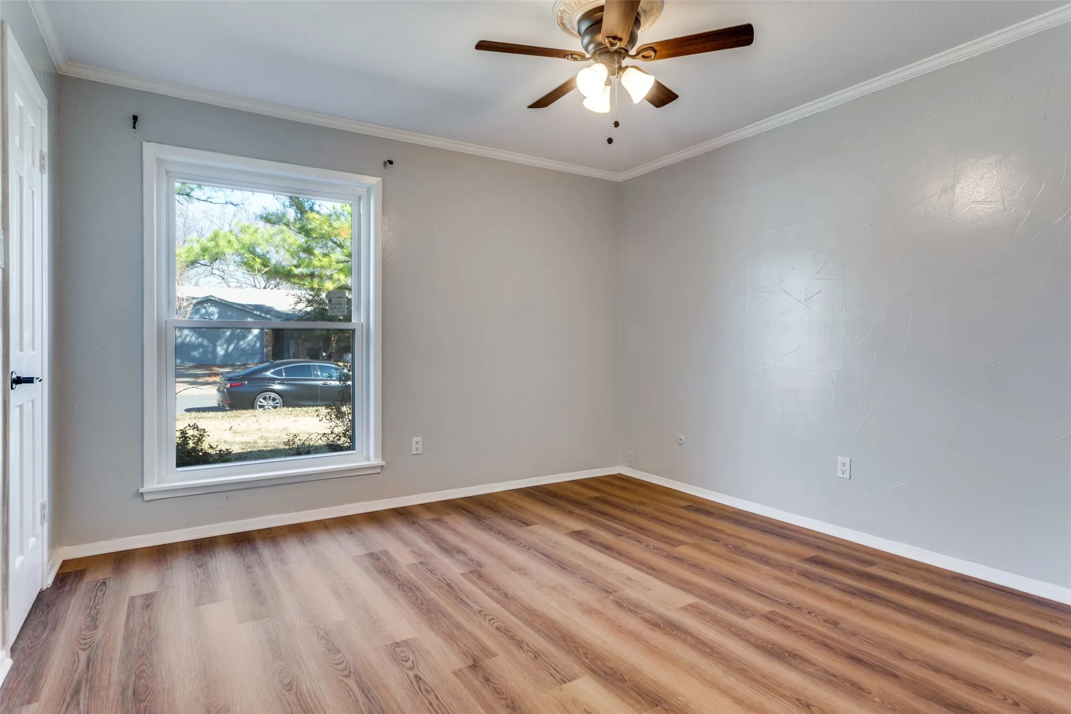 Room featuring wood-finish flooring, a double-hung window with white trim, and a ceiling fan with integrated lighting