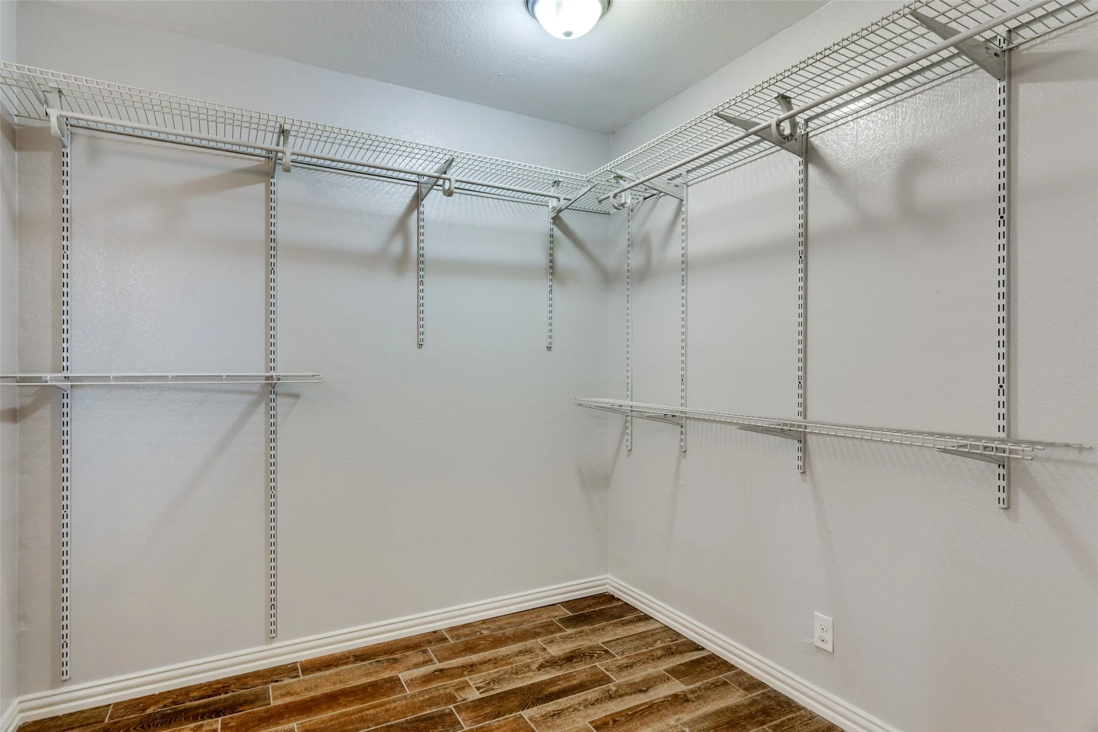 Expansive closet featuring wire shelving, wire hanging rods, ceiling-mounted lighting, and wood-finish flooring