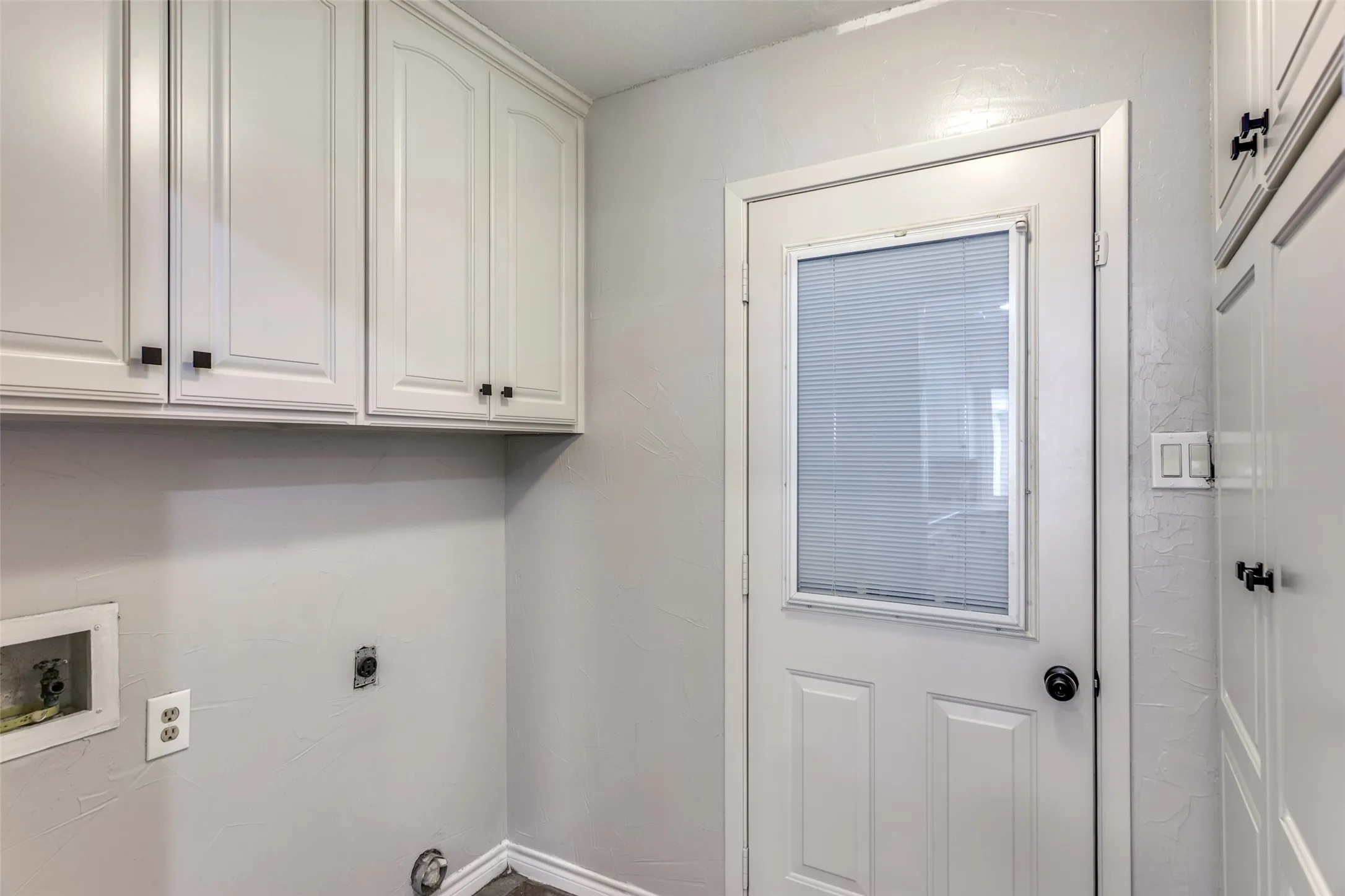 Utility space featuring shaker-style cabinetry with matte black hardware, a light-colored wall finish, and a door with an integrated privacy blind
