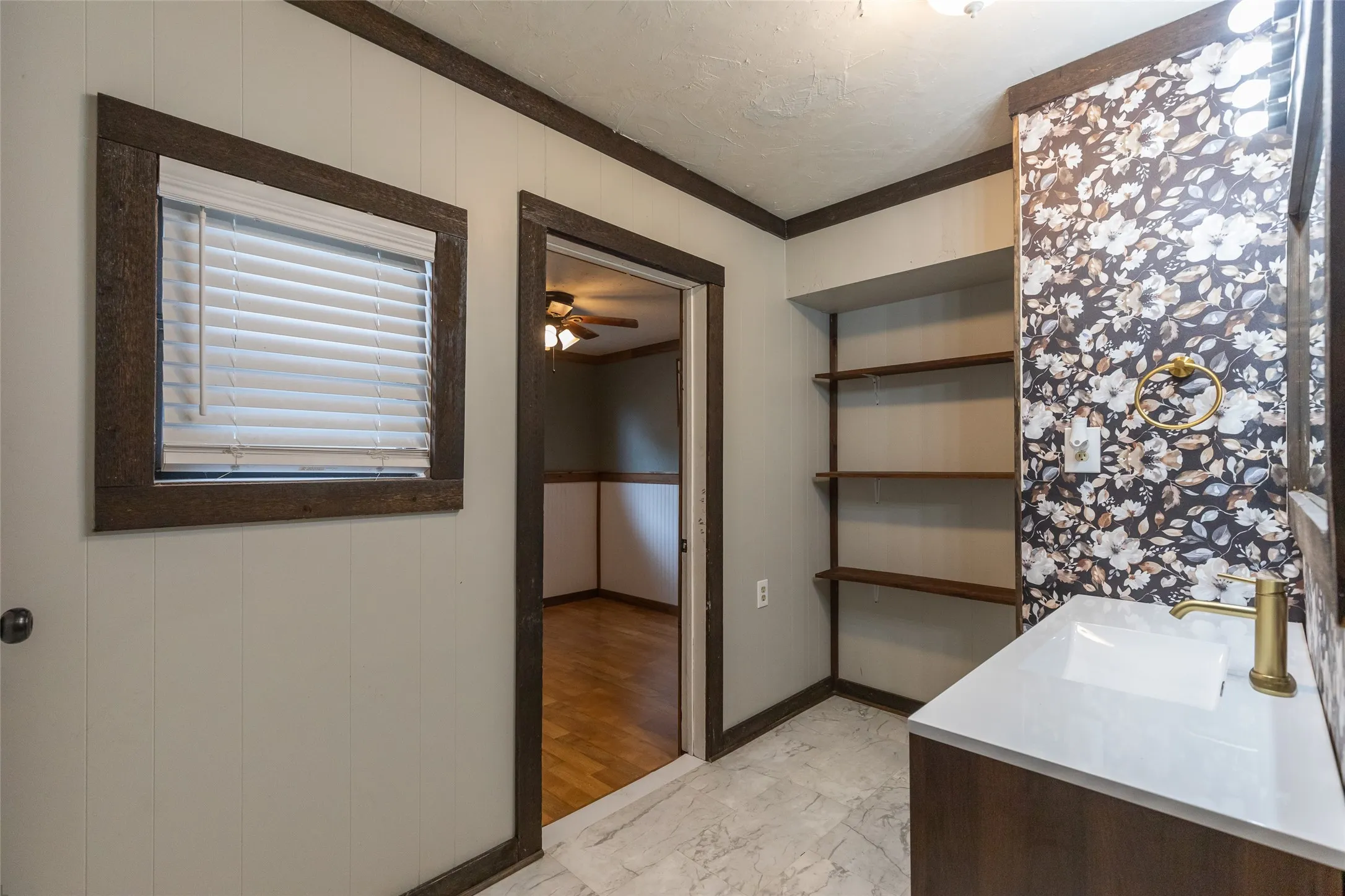 Bathroom featuring a dark wood-finish vanity with a white rectangular sink and gold-tone faucet, complemented by patterned wallpaper