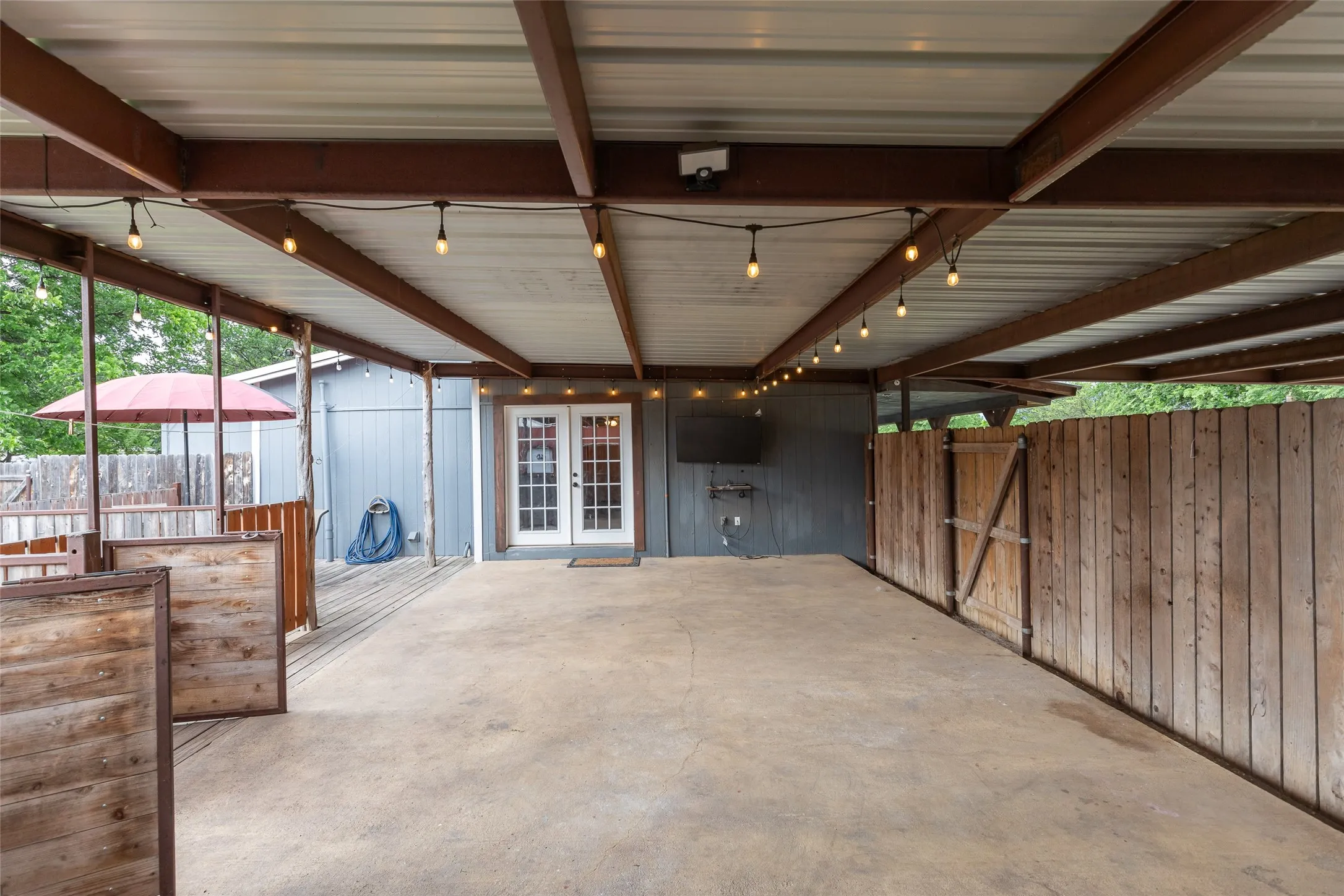 Covered concrete patio with string lighting, direct access via French doors, and a wood privacy fence