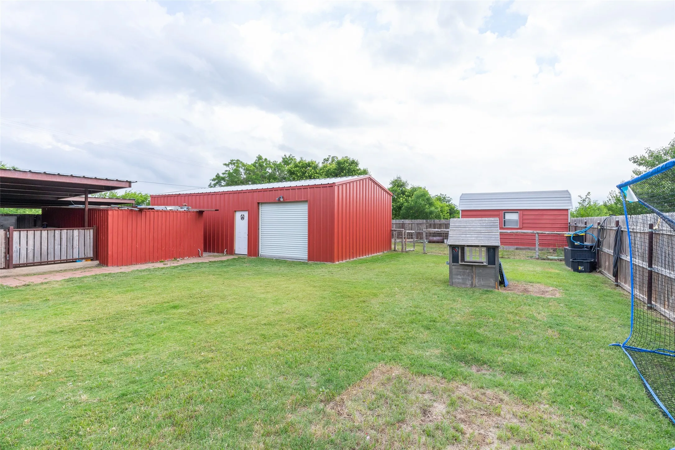 Expansive rear yard featuring multiple red metal outbuildings, and a perimeter fence