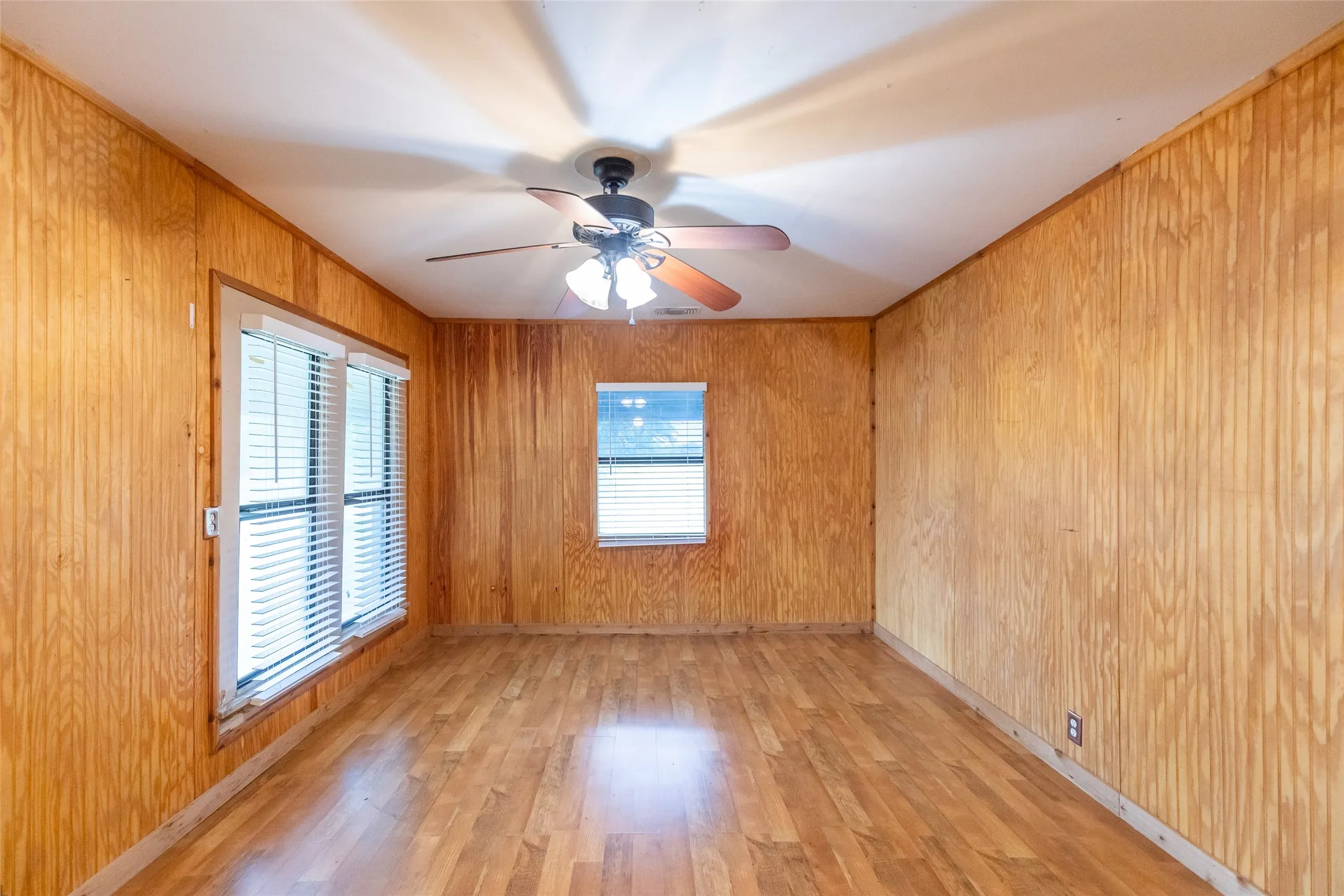 Interior room featuring wood-panel walls, wood-finish flooring, and white trim windows