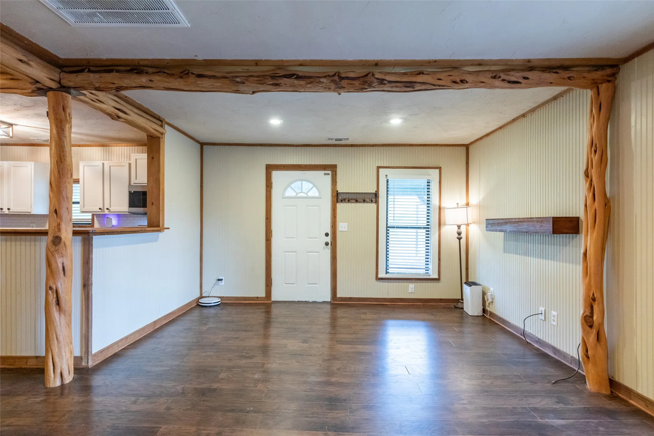 Open-concept living area featuring wood-finish flooring, a white paneled entry door with an arched window, and a window with blinds