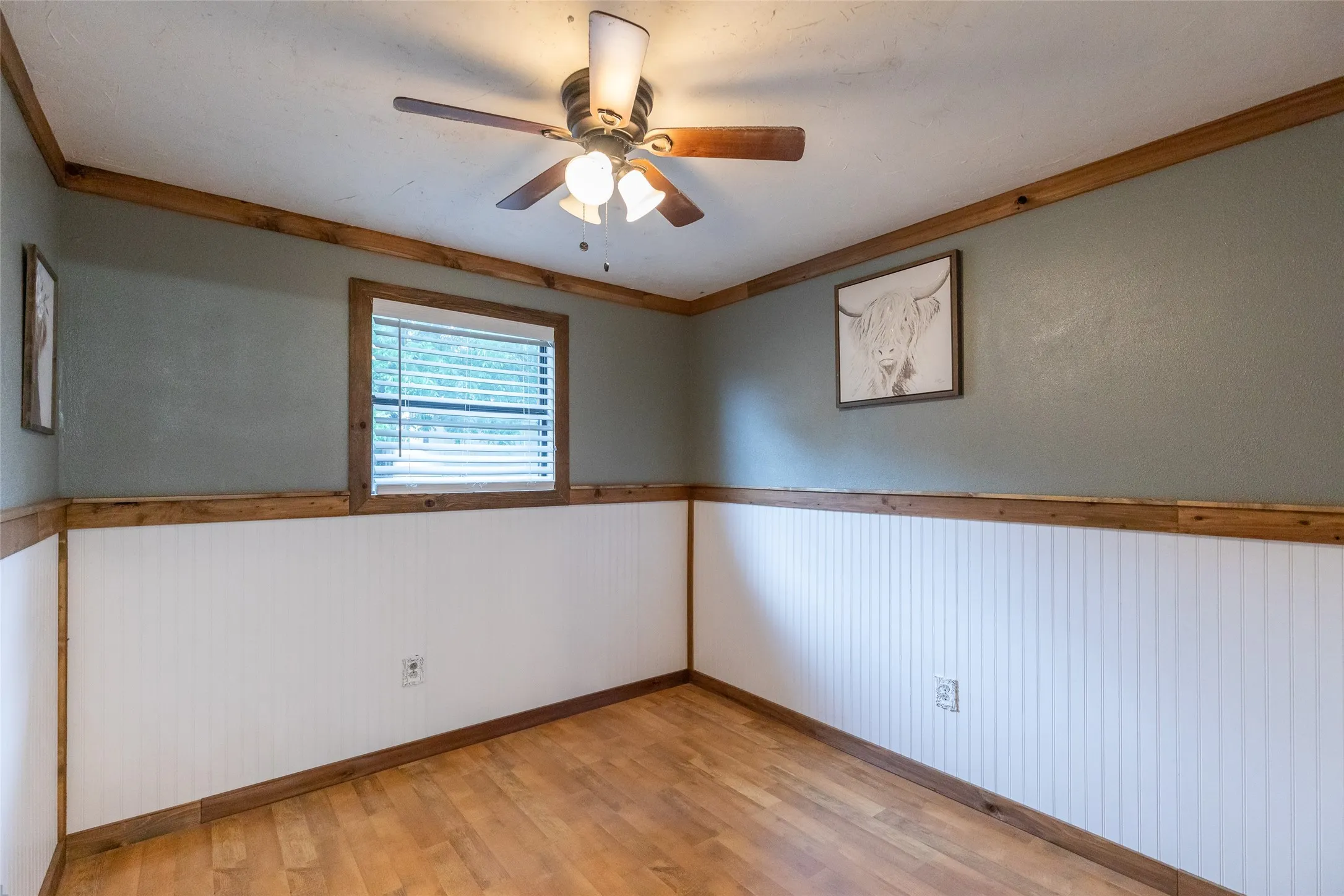 Room featuring wood-finish flooring, white beadboard wainscoting, and a ceiling fan with integrated lighting