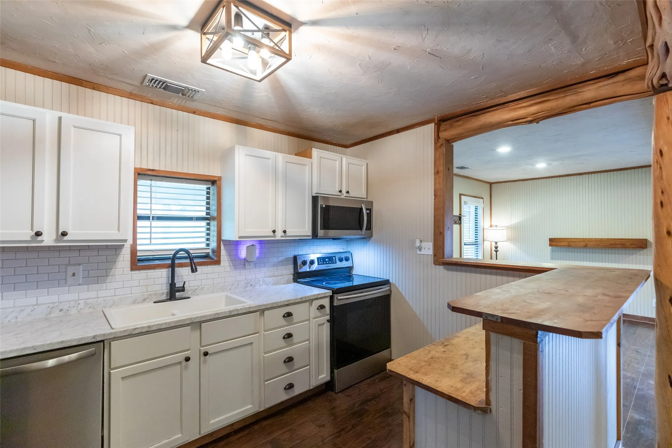 Kitchen featuring white shaker cabinetry, white subway tile backsplash, stainless steel appliances, a white rectangular sink with a matte black faucet, and a pass-through bar with a wood-finish countertop