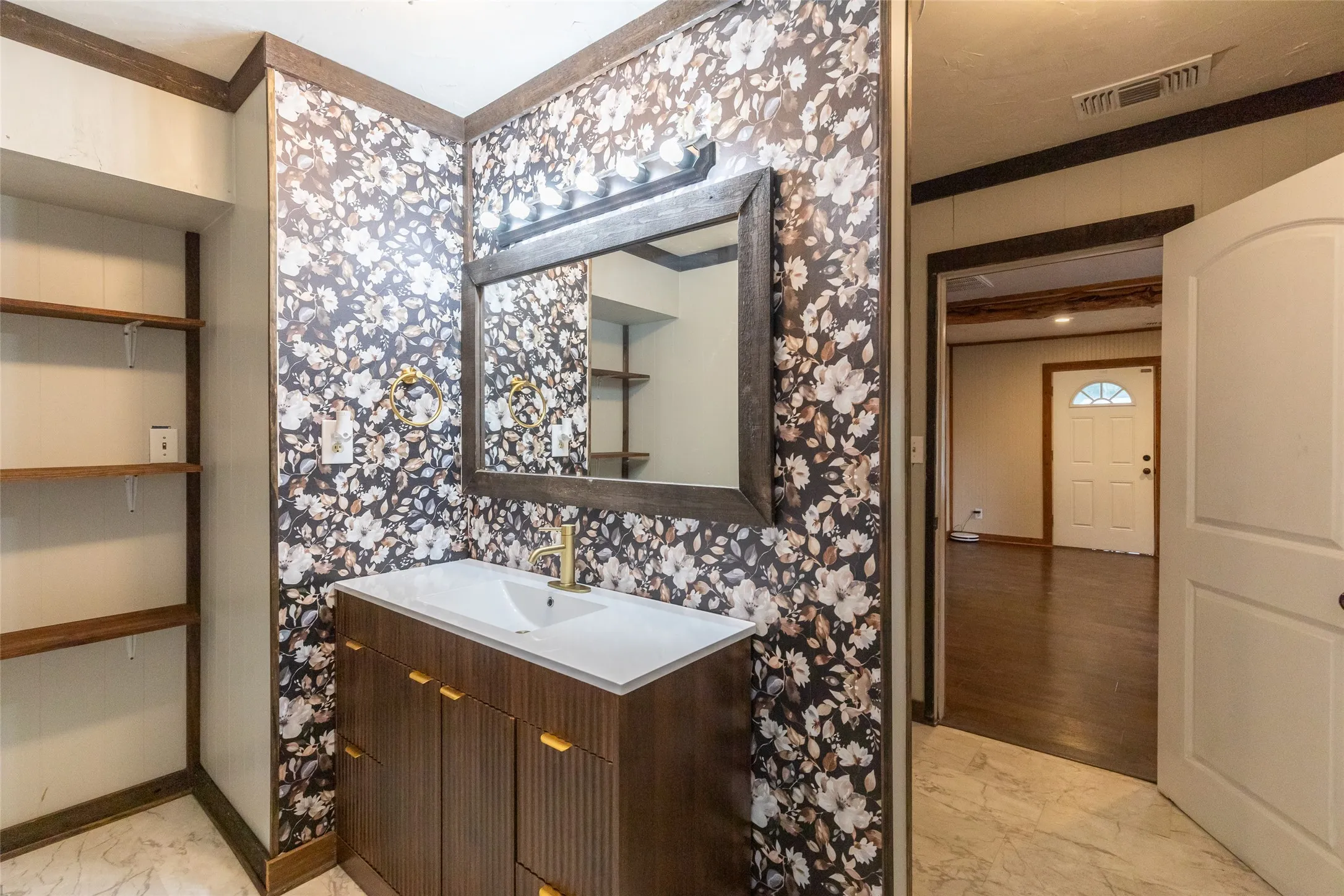 Vanity area featuring a wood-finish cabinet with gold-tone hardware, white countertop with integrated sink, and gold-tone faucet