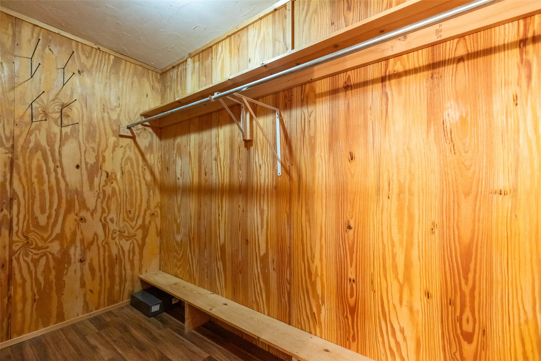 Primary closet with wood-finish flooring, paneled walls, a built-in shelf, and a clothing rod
