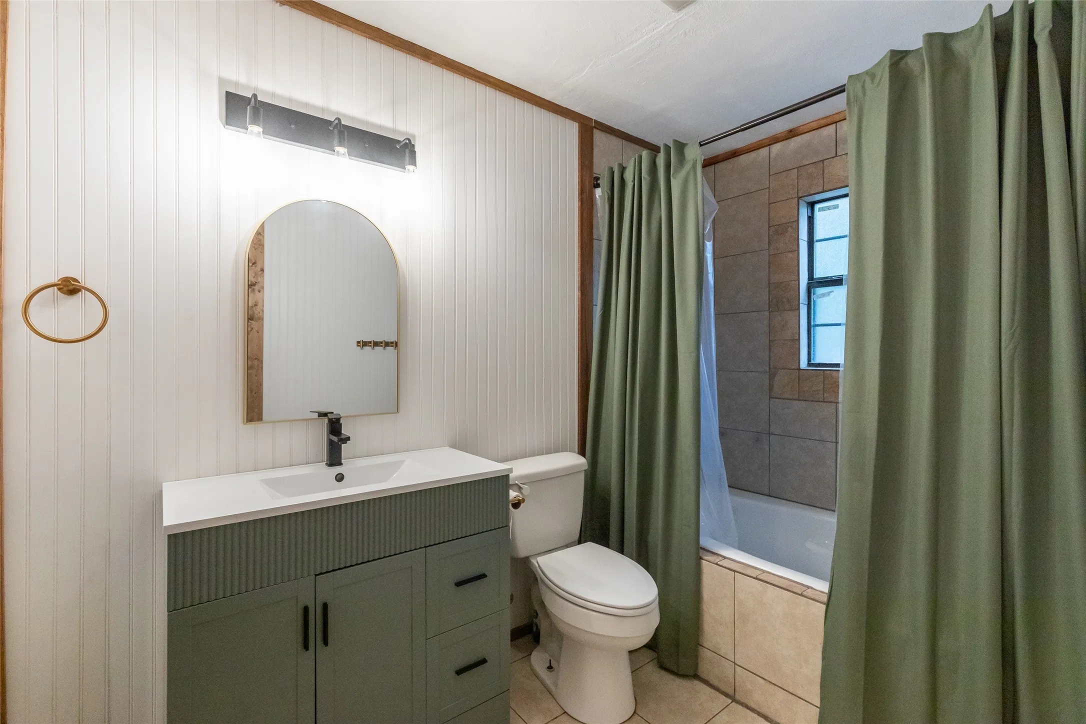 Bathroom featuring a green vanity with a white countertop, an arched framed mirror, and a wall-mounted light fixture