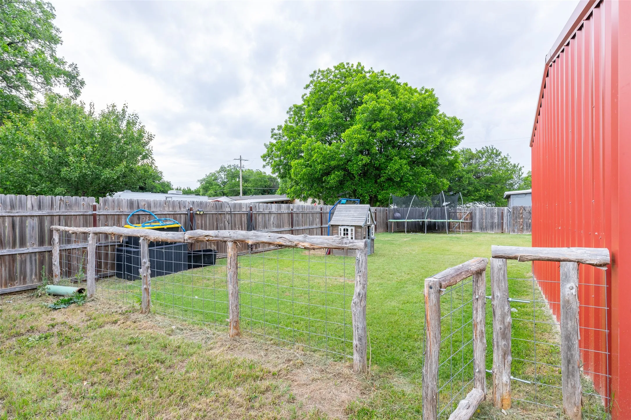 Expansive outdoor space featuring a red metal-sided structure, a wood privacy fence, and a grassy lawn