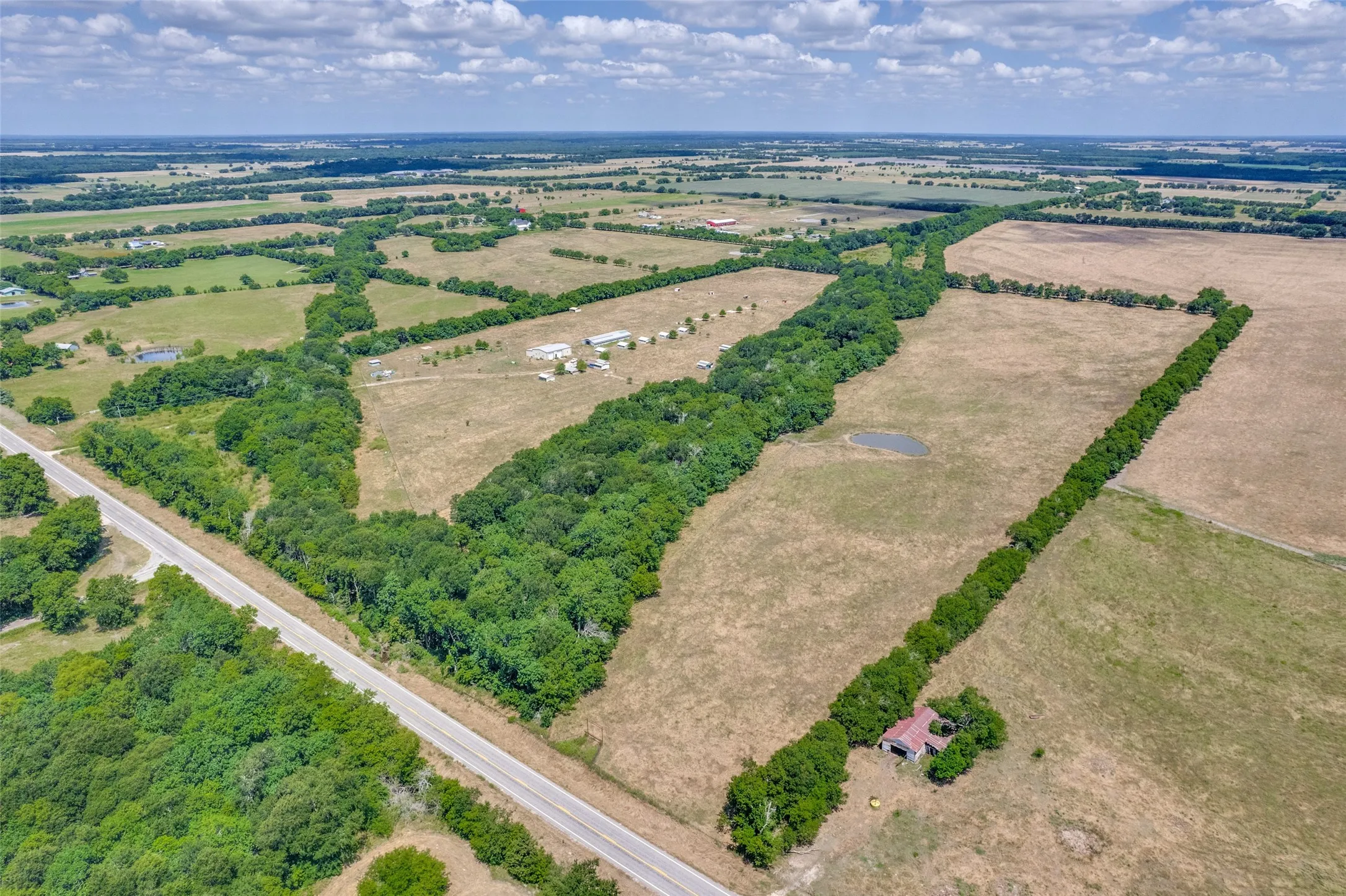 Expansive acreage featuring a paved road frontage of FM 1563 ,established tree lines, open fields, and a visible pond