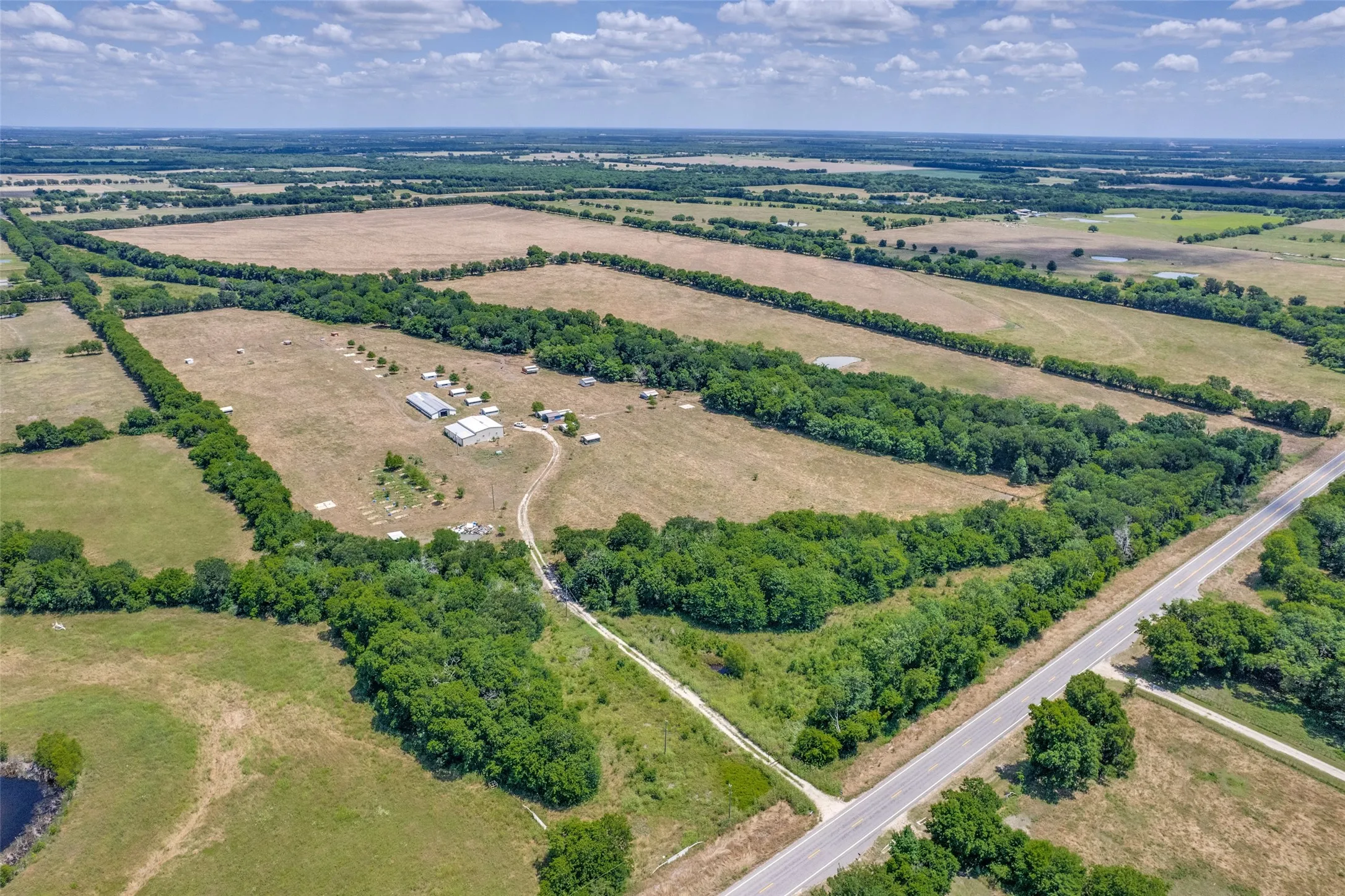 Expansive rural property featuring multiple cleared sections, dense tree lines, a paved road frontage, and a visible pond