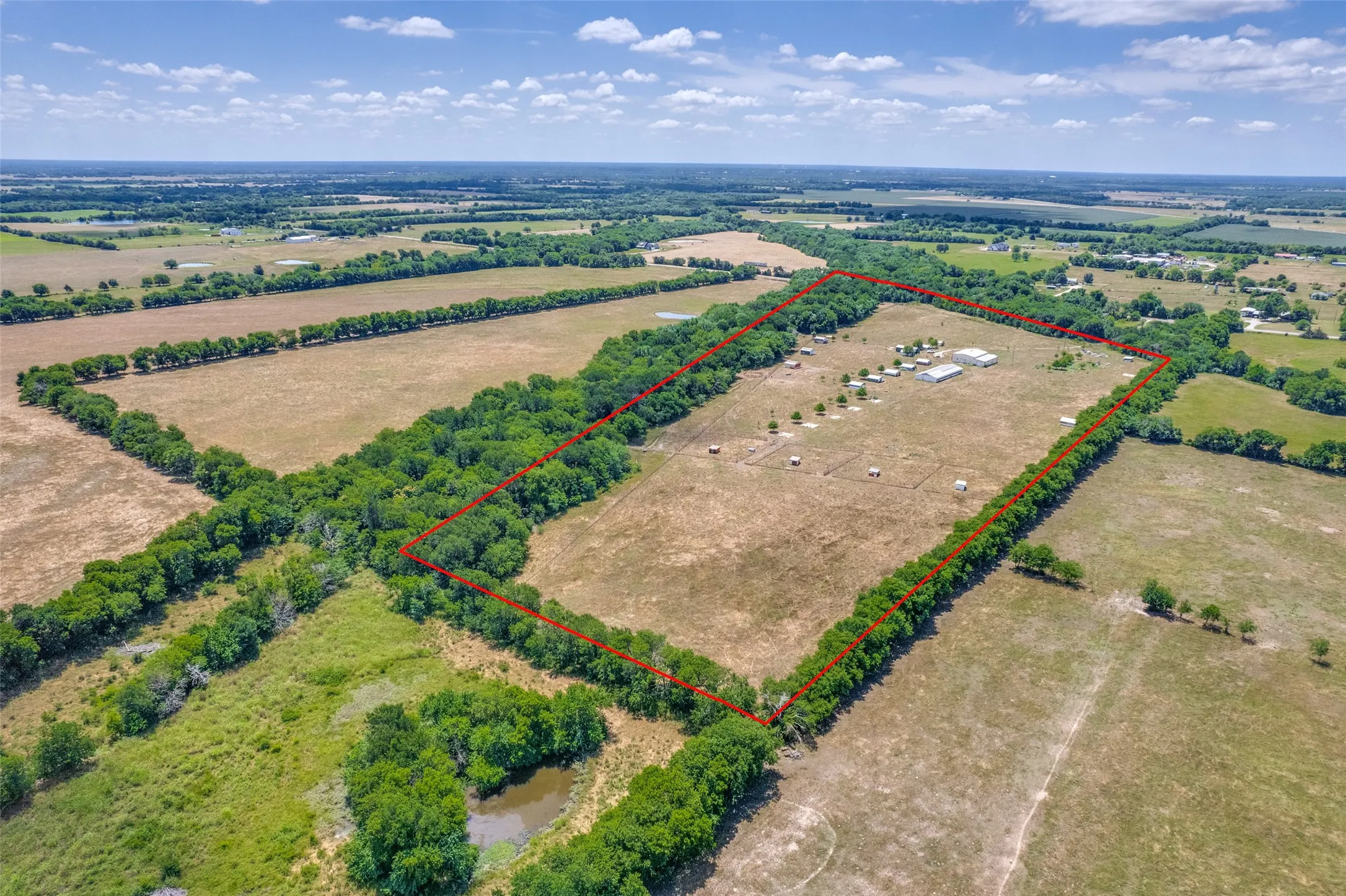 Expansive acreage featuring multiple structures, mature tree lines, and a pond