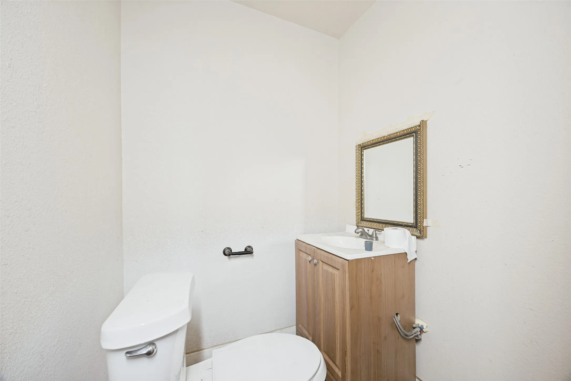White water closet featuring a porcelain toilet, wood-finish vanity with an integrated sink, and an ornate framed mirror