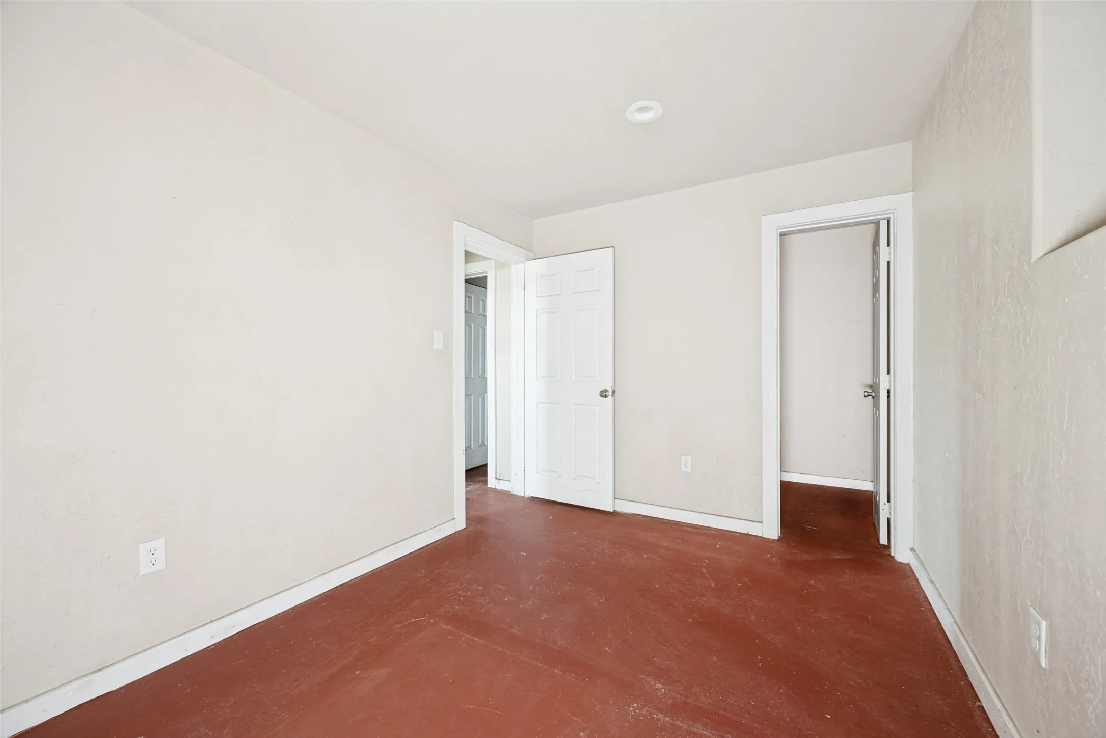 Spacious interior room featuring light-toned walls, contrasting dark flooring, recessed ceiling lighting, and multiple interior doorways