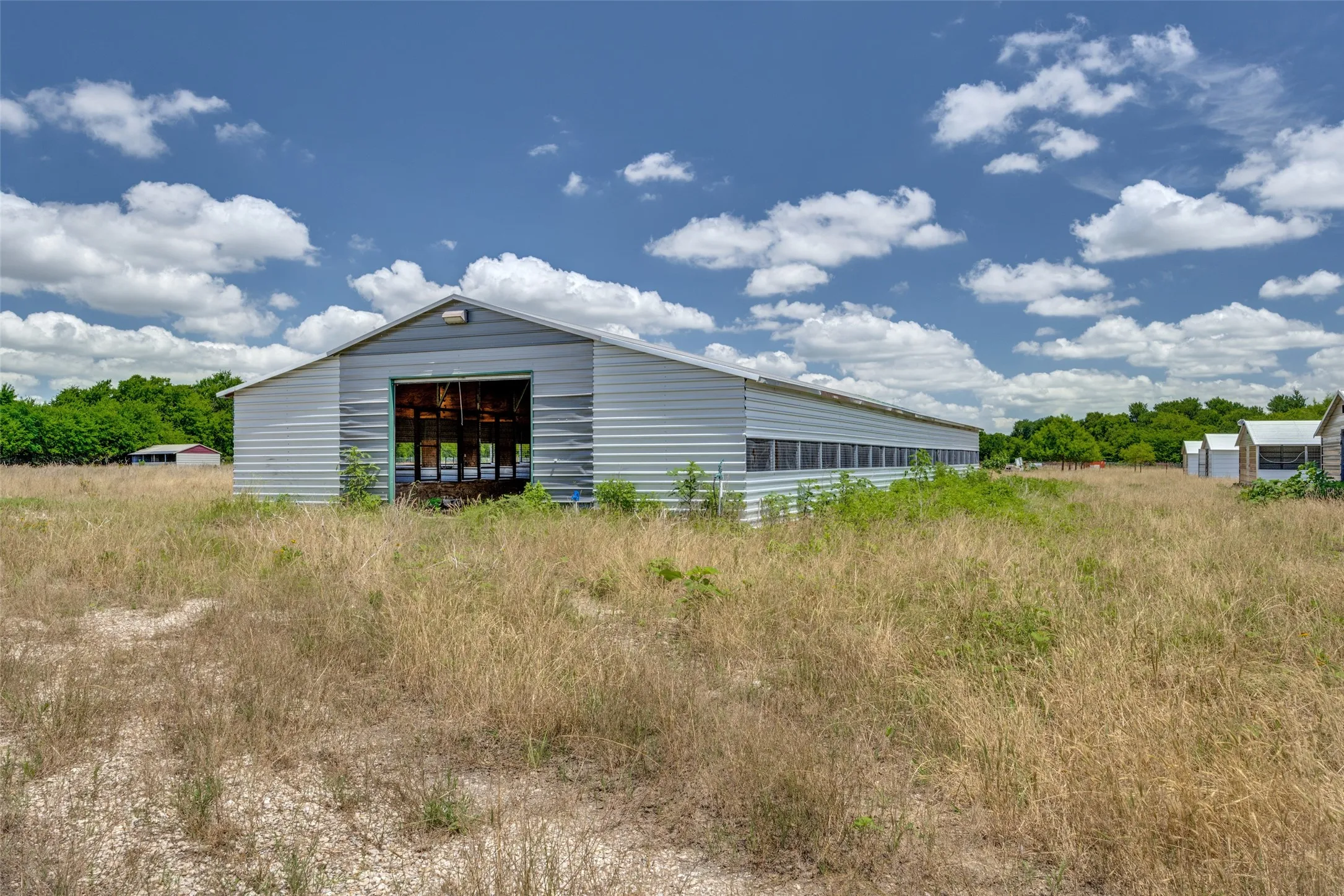 Long metal-sided barn featuring a large open doorway and multiple side windows