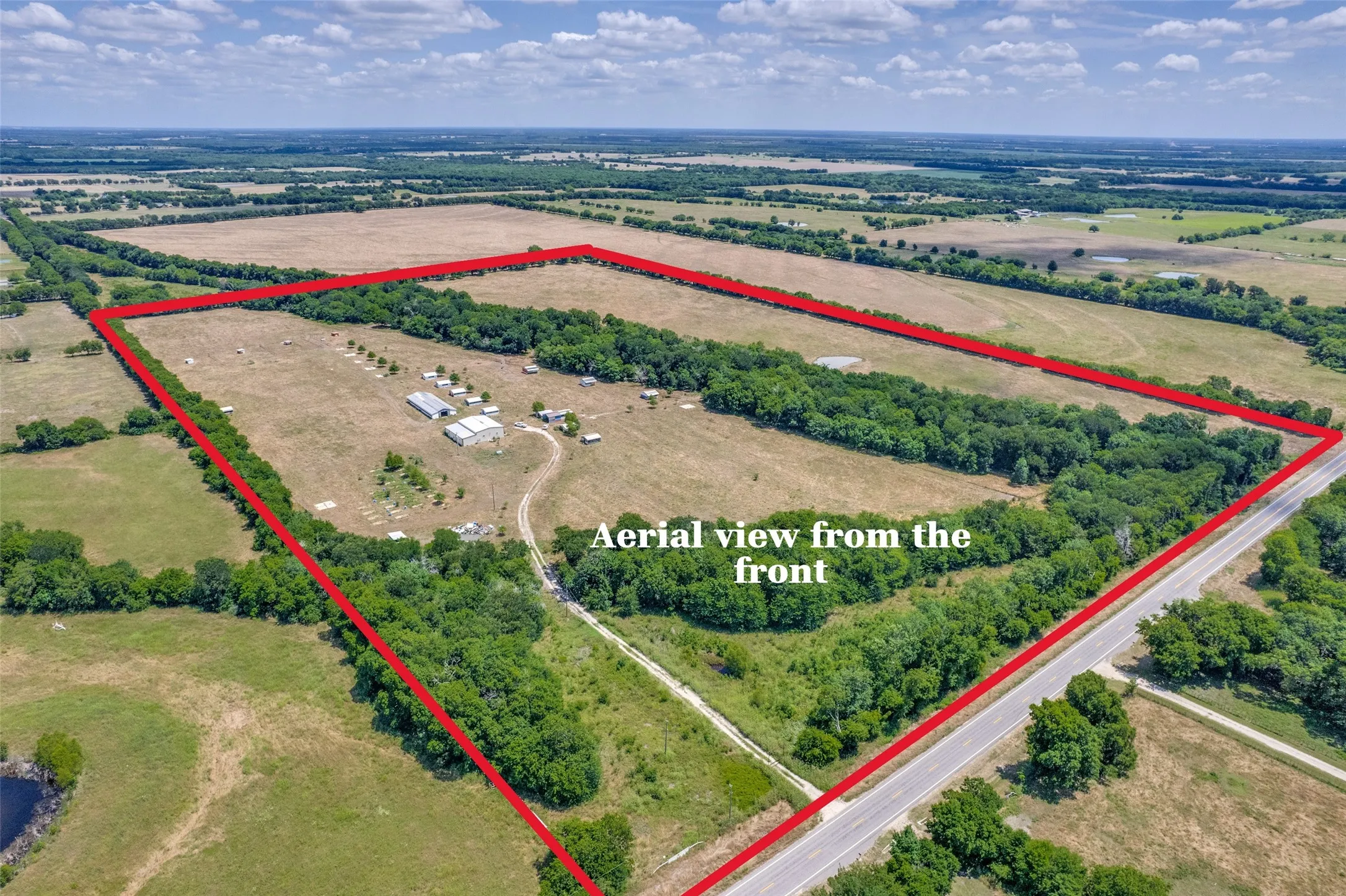 Expansive rural property featuring a paved road frontage, natural tree lines, multiple outbuildings, and open land