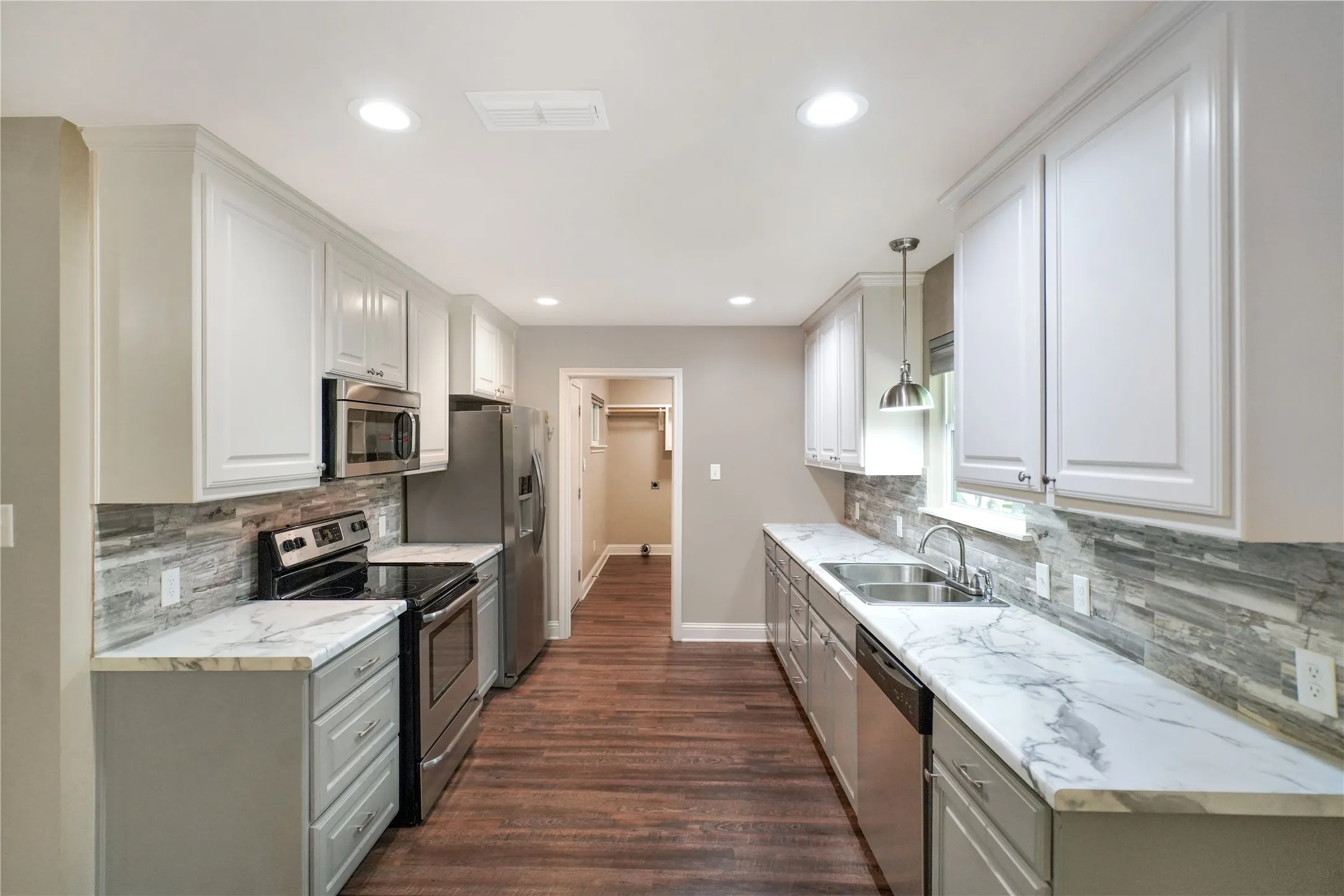 Kitchen featuring white upper cabinetry, gray lower cabinetry, stainless steel appliances, wood-finish flooring, and light-toned countertops with distinctive veining