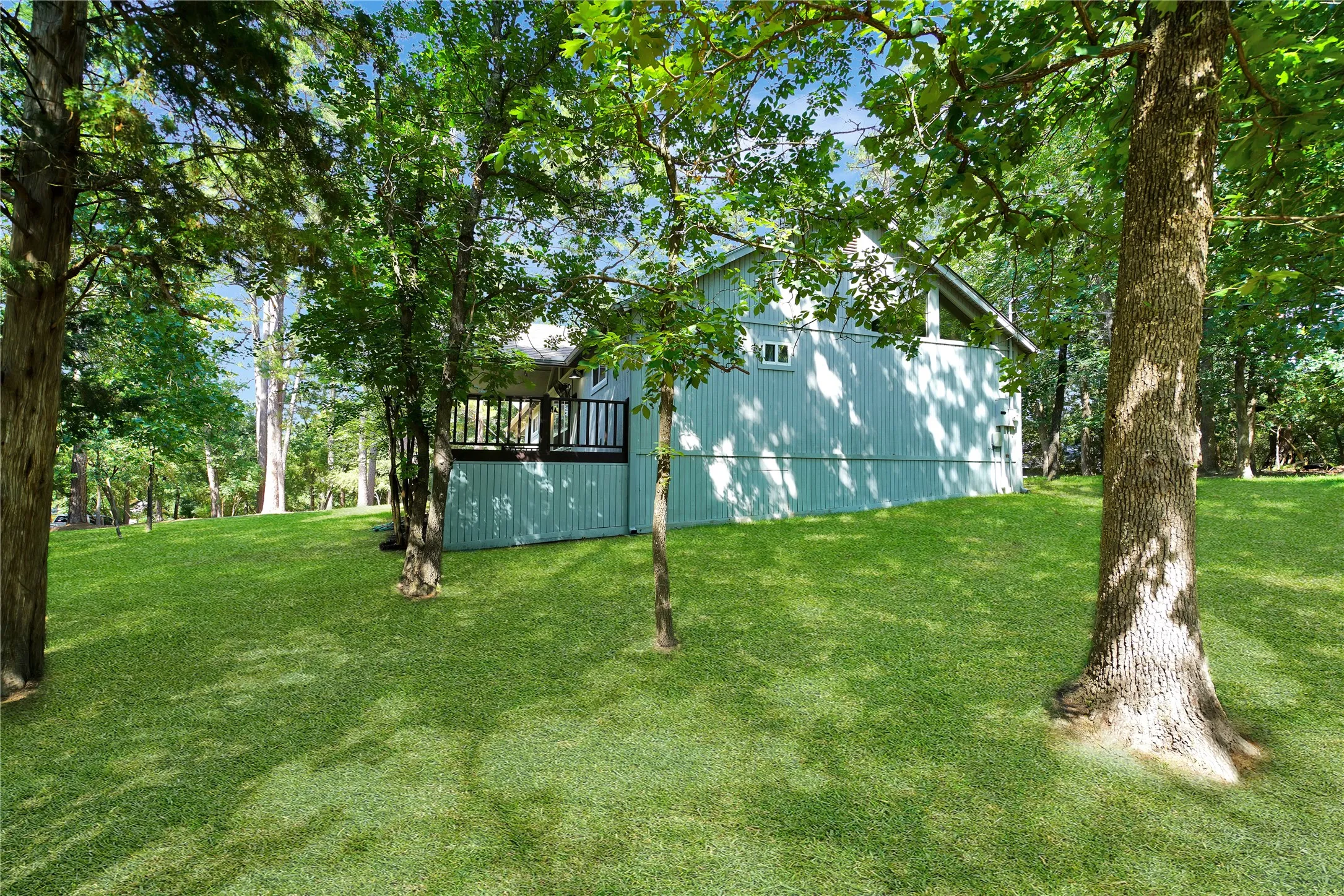 Expansive green lawn surrounds the property, featuring mature trees and a rear deck with black railings