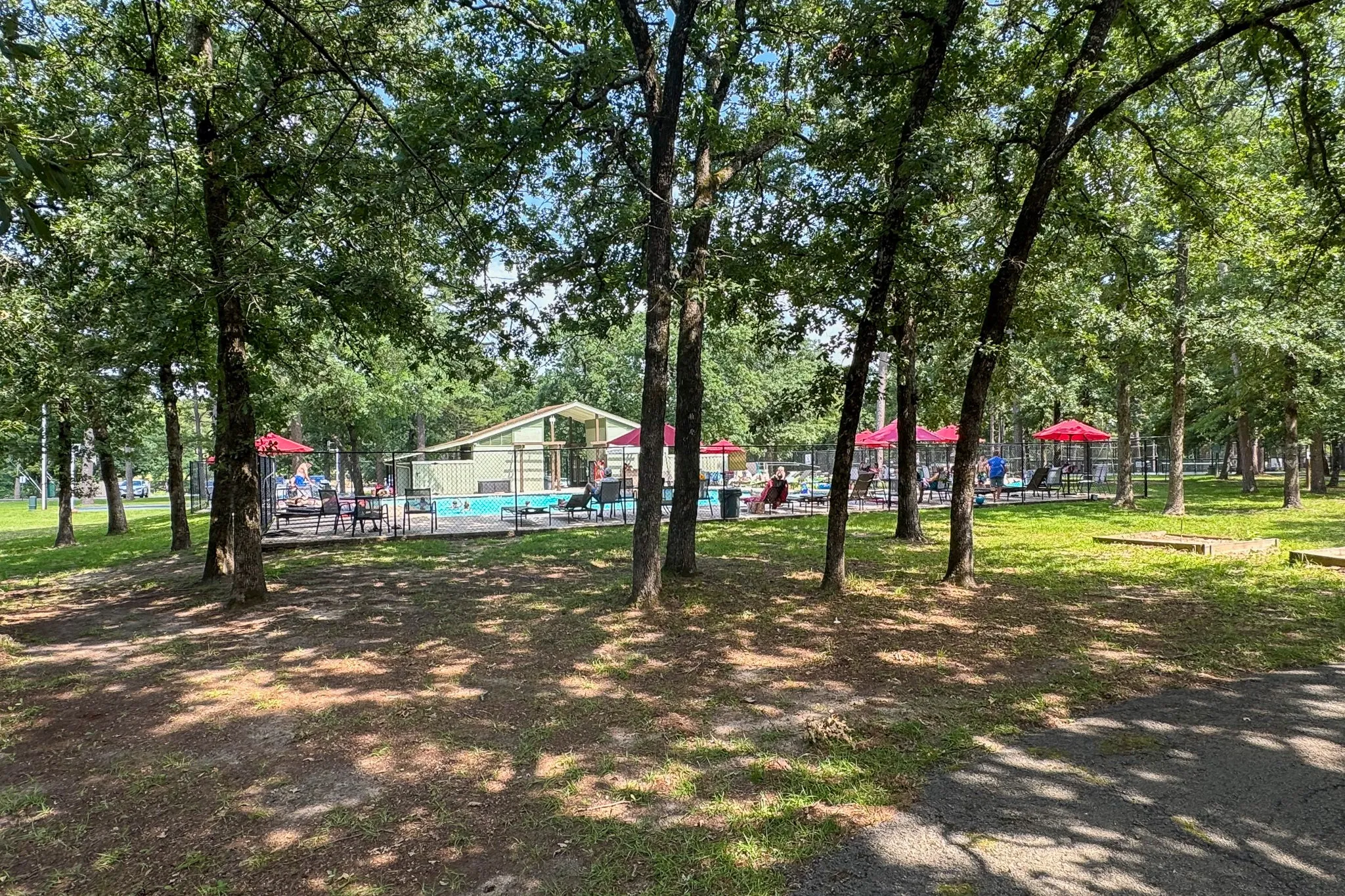 Outdoor swimming pool area with a surrounding fence, featuring multiple lounge chairs and red umbrellas