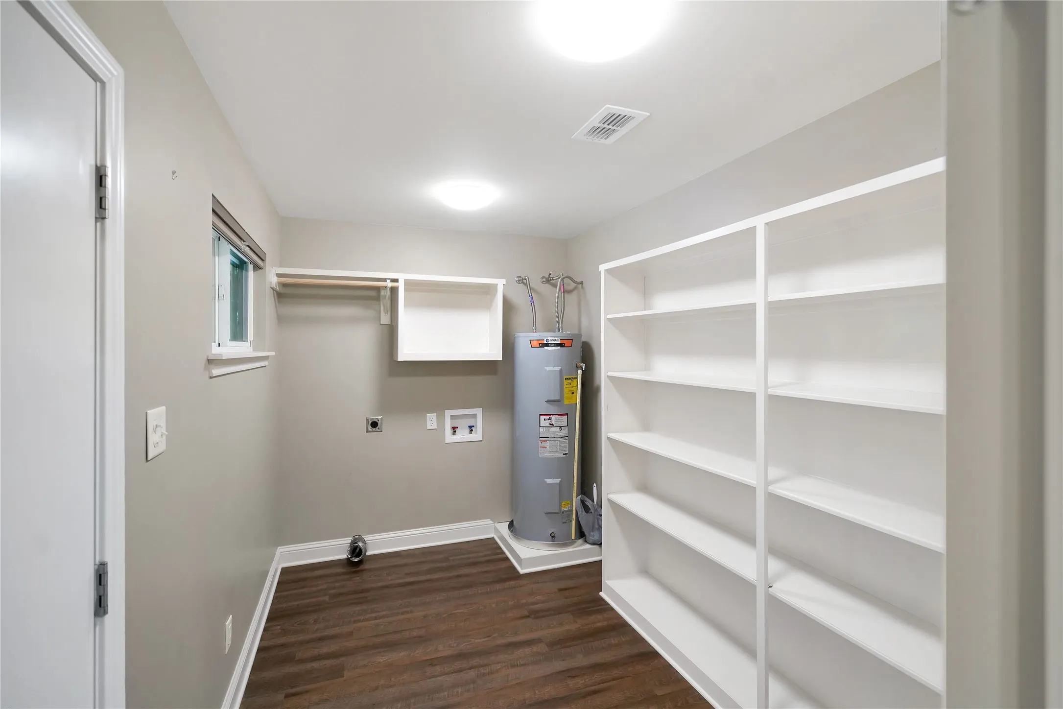 Dedicated utility area featuring wood-finish flooring, built-in shelving, a wall-mounted clothing rod, and water heater