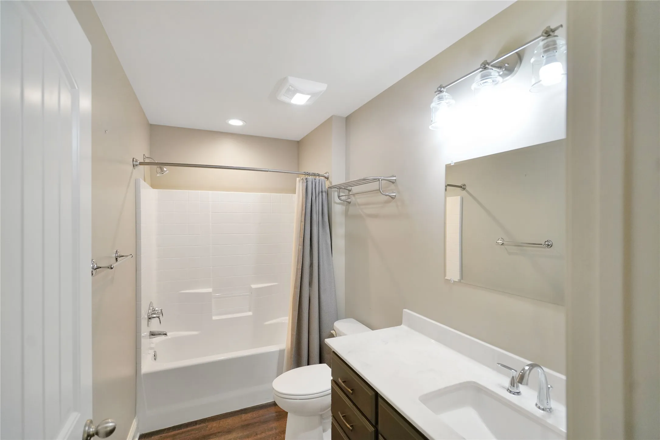 Bathroom featuring wood-finish flooring, a white vanity with an integrated sink and chrome faucet, a rectangular mirror, and a white tub with subway tile surround