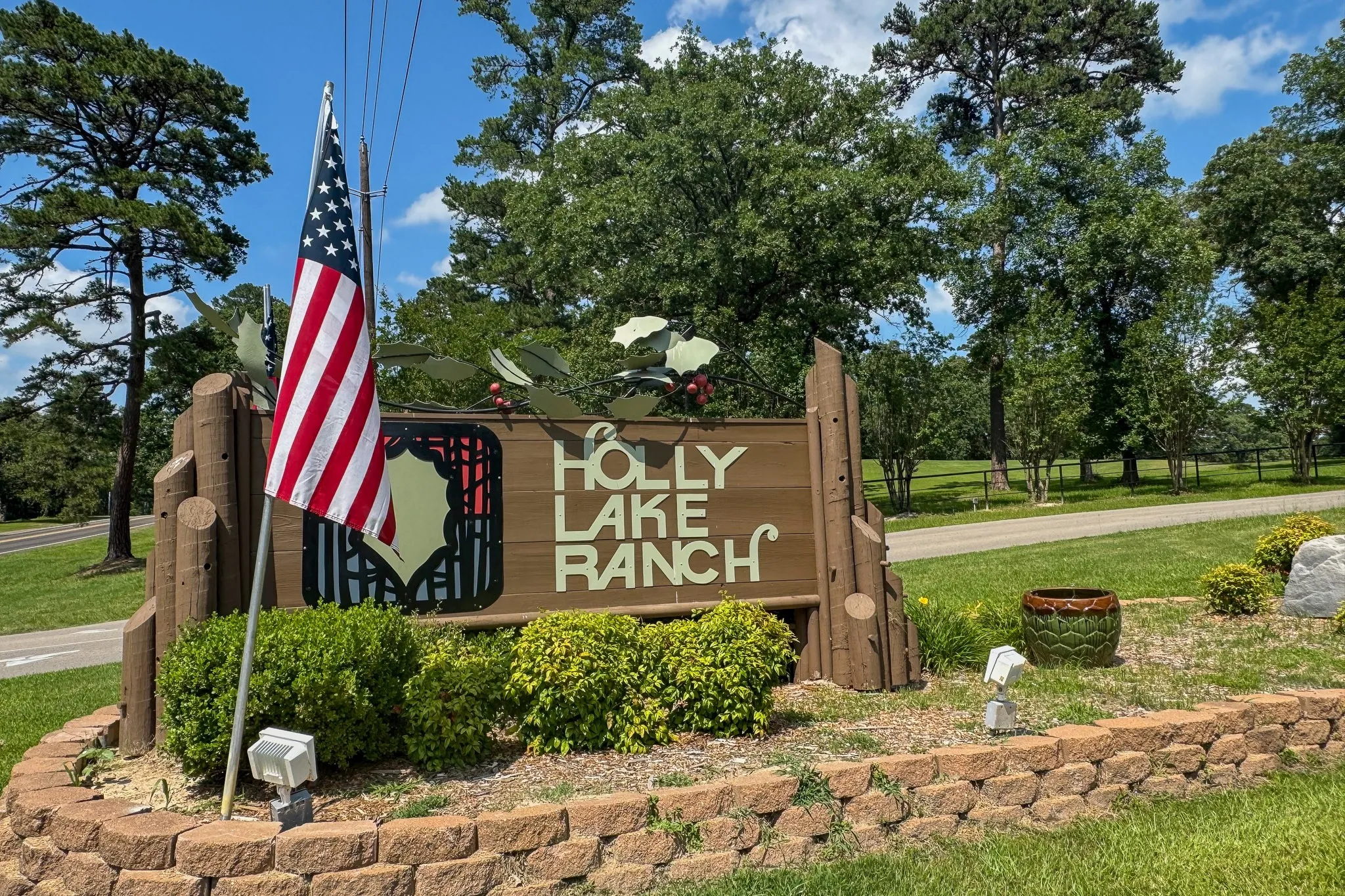 Entry sign featuring "Holly Lake Ranch" lettering on wood-finish material, surrounded by manicured landscaping
