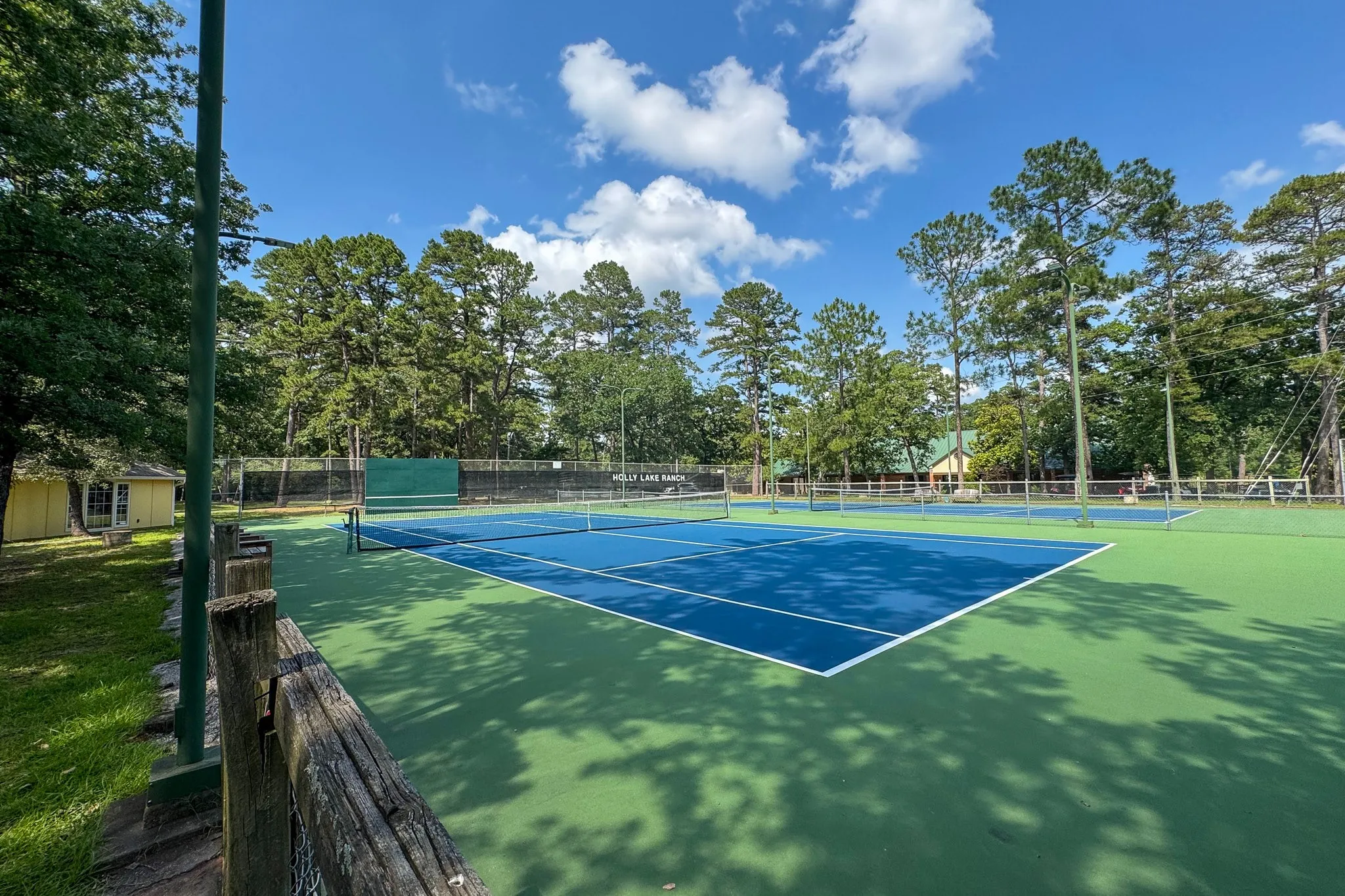 Hard surface tennis court featuring a blue playing area and green surrounds