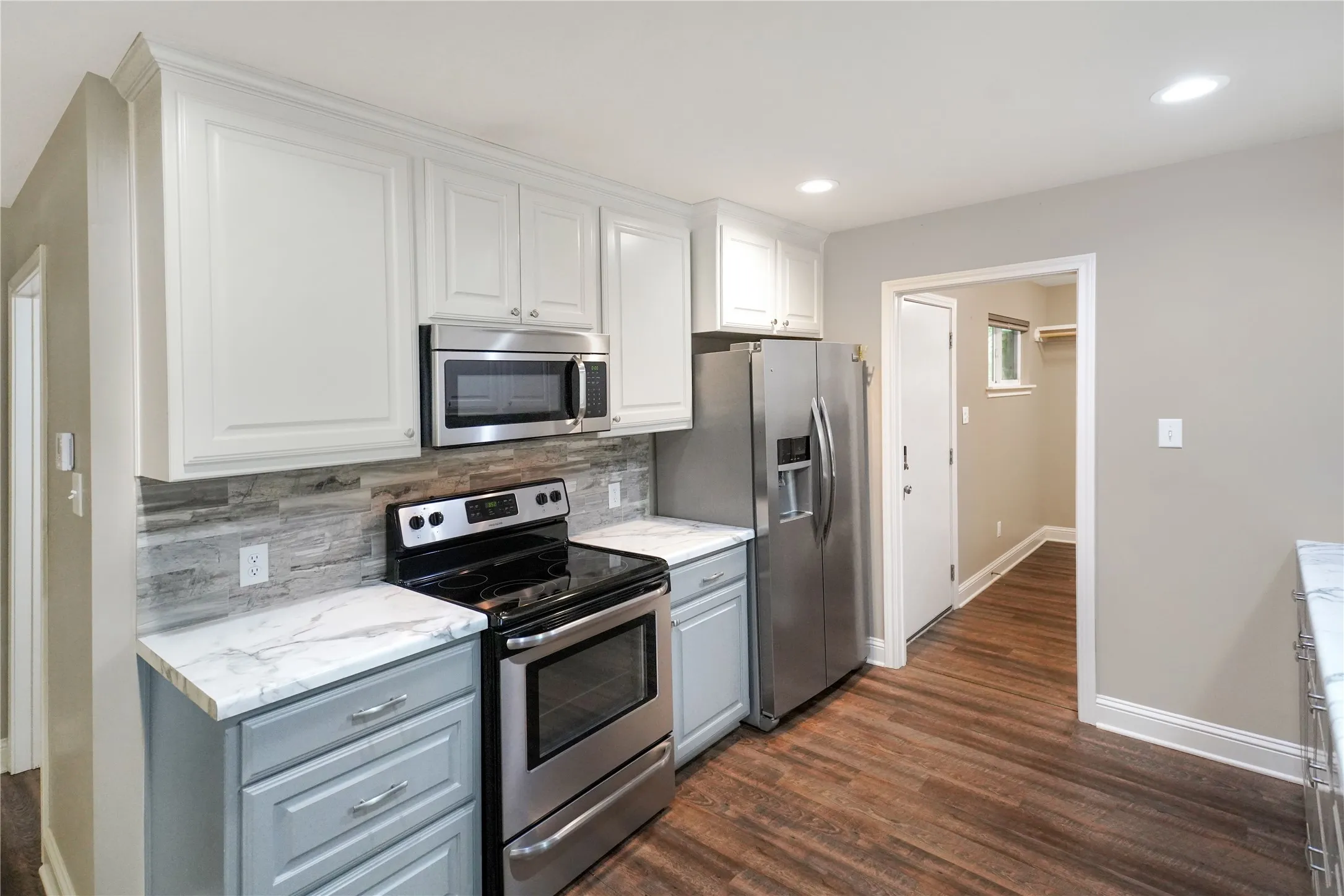 Kitchen featuring stainless steel appliances, wood-finish flooring, white upper cabinetry, light gray lower cabinetry, and stone-look countertops