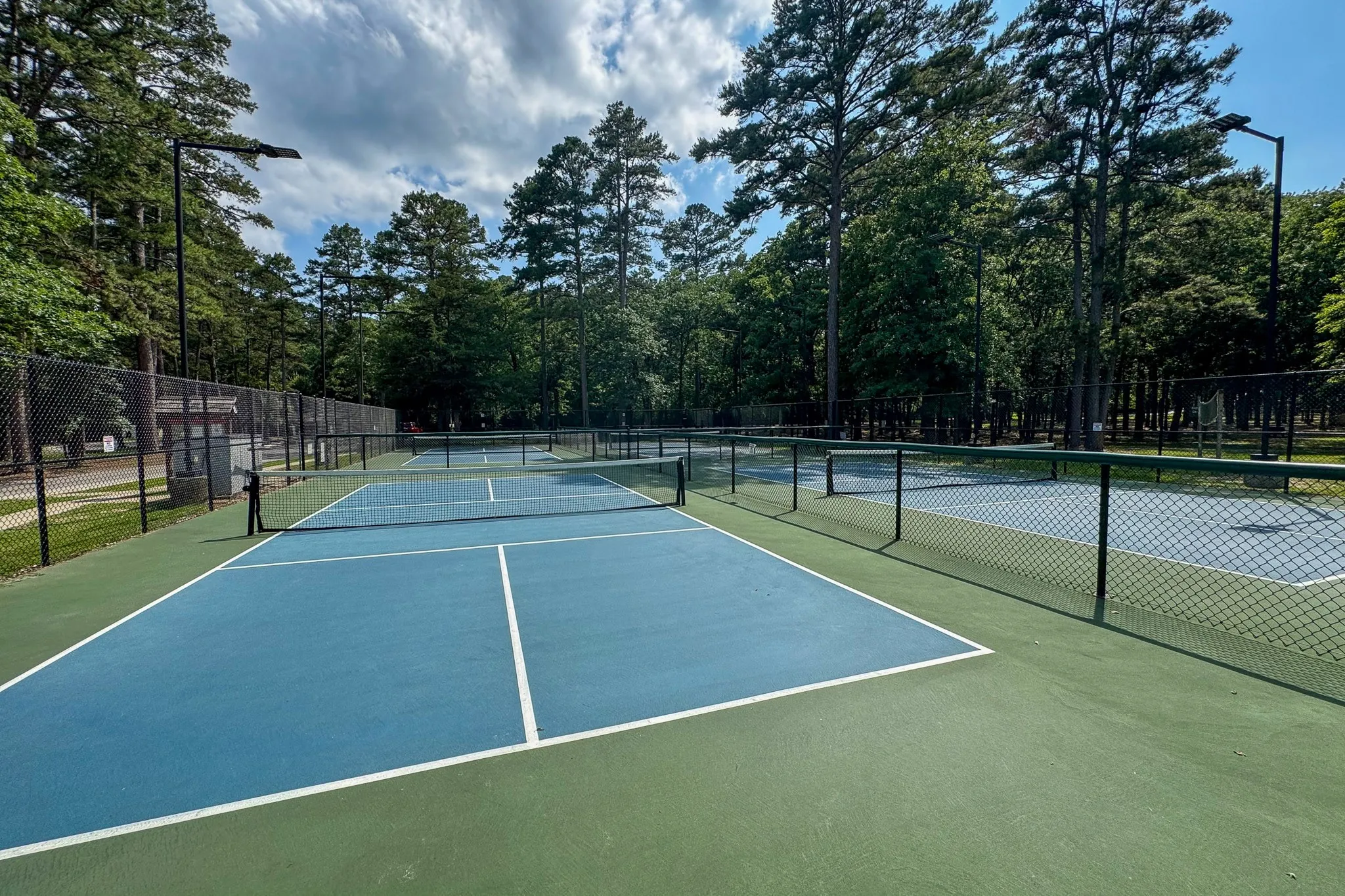 Multiple outdoor courts featuring blue playing surfaces with white line markings, surrounded by green perimeters