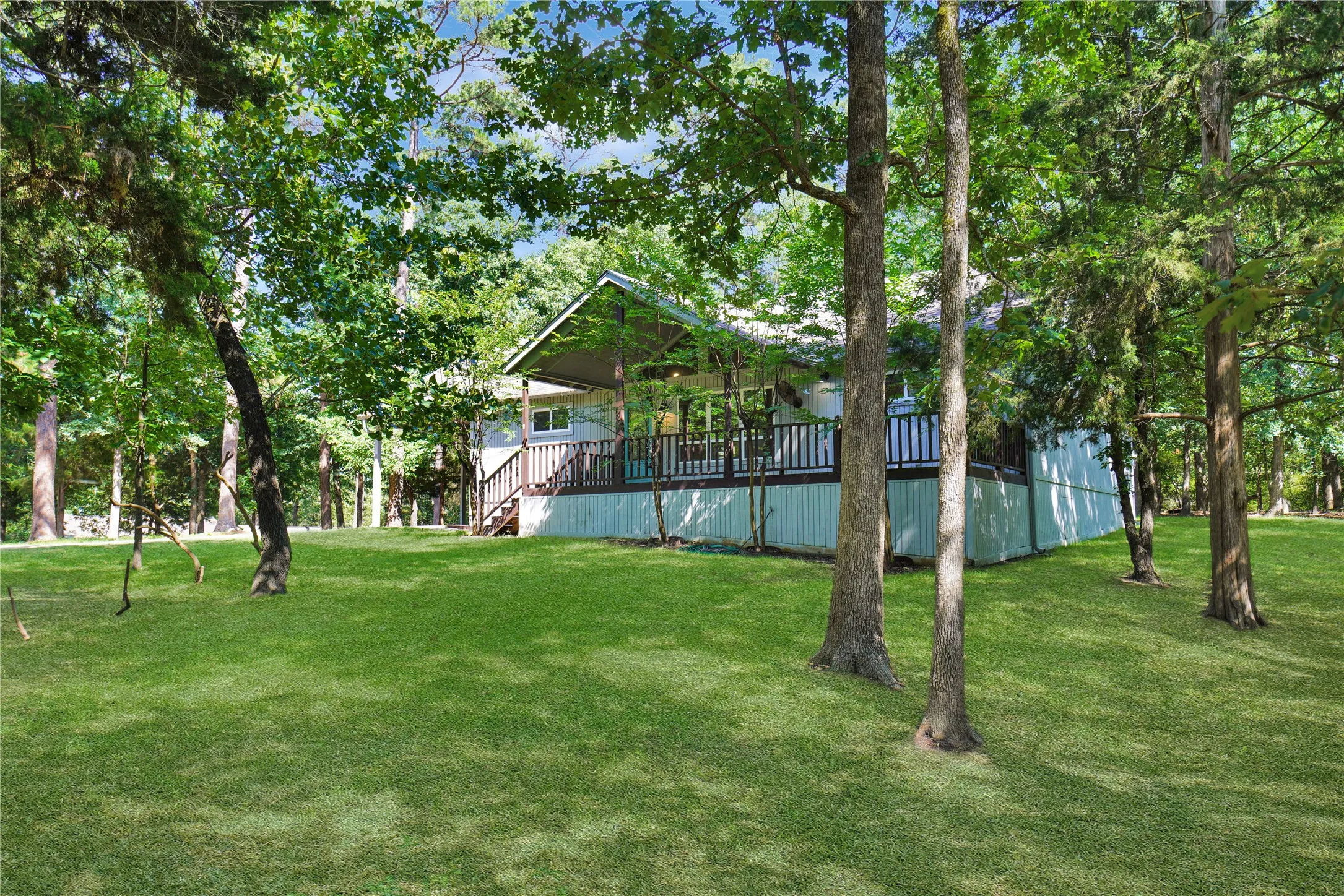 Expansive green lawn surrounds a property featuring a covered porch with dark railings and steps