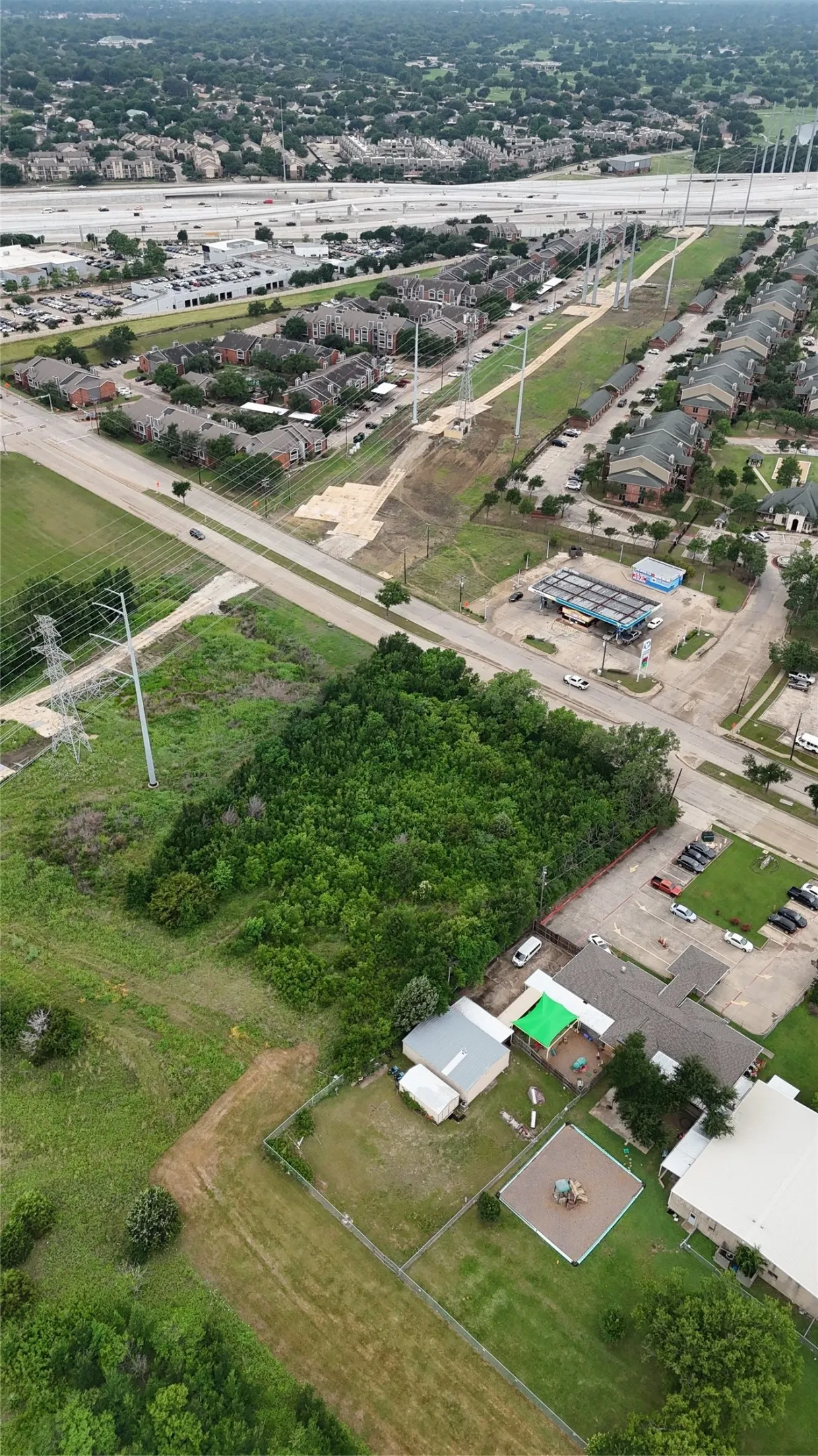 Expansive land parcel featuring dense tree coverage, bordered by a paved road and commercial structures