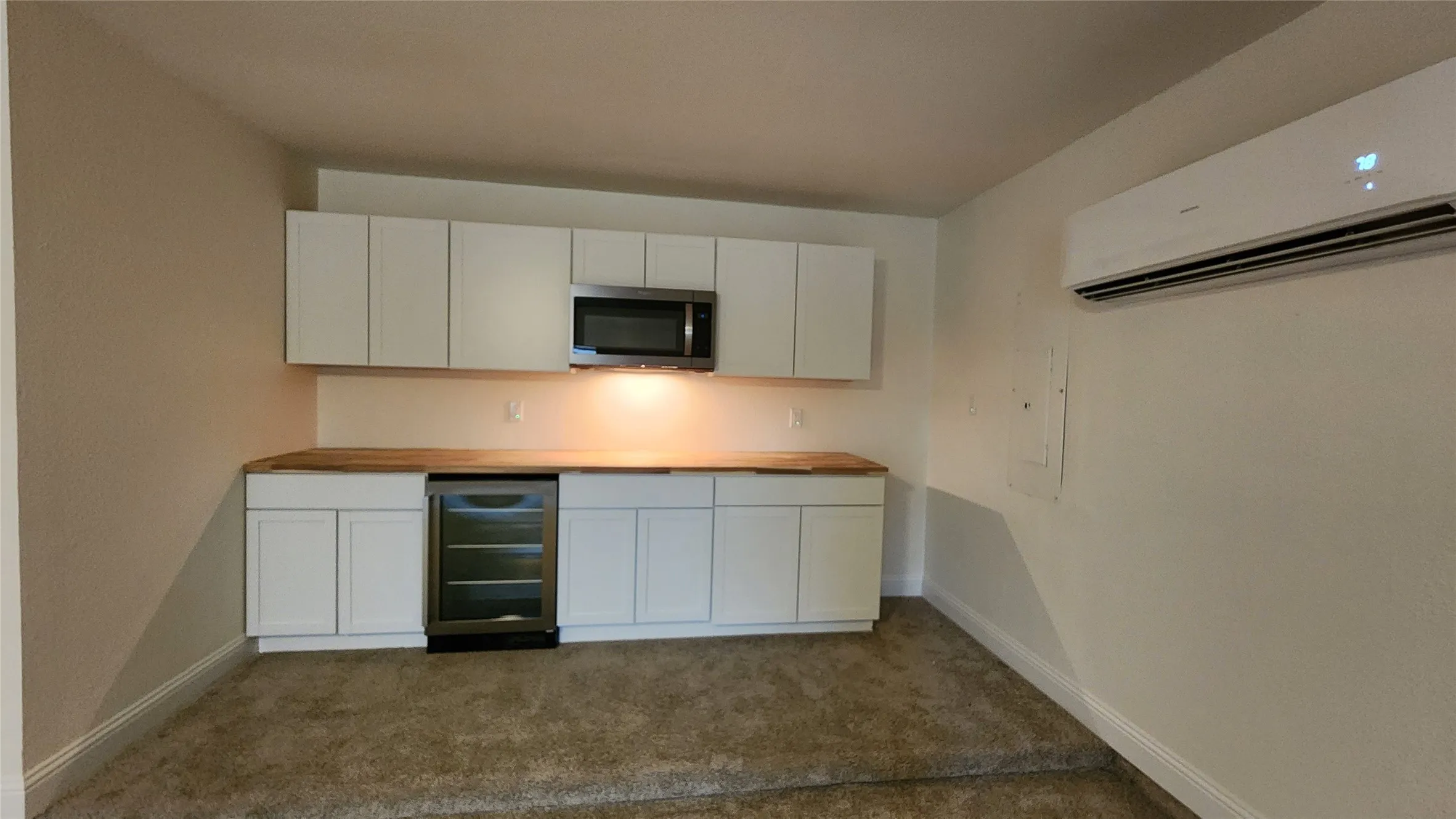 Kitchen with wine cooler, a wall mounted air conditioner, butcher block counters, stainless steel microwave, and dark colored carpet