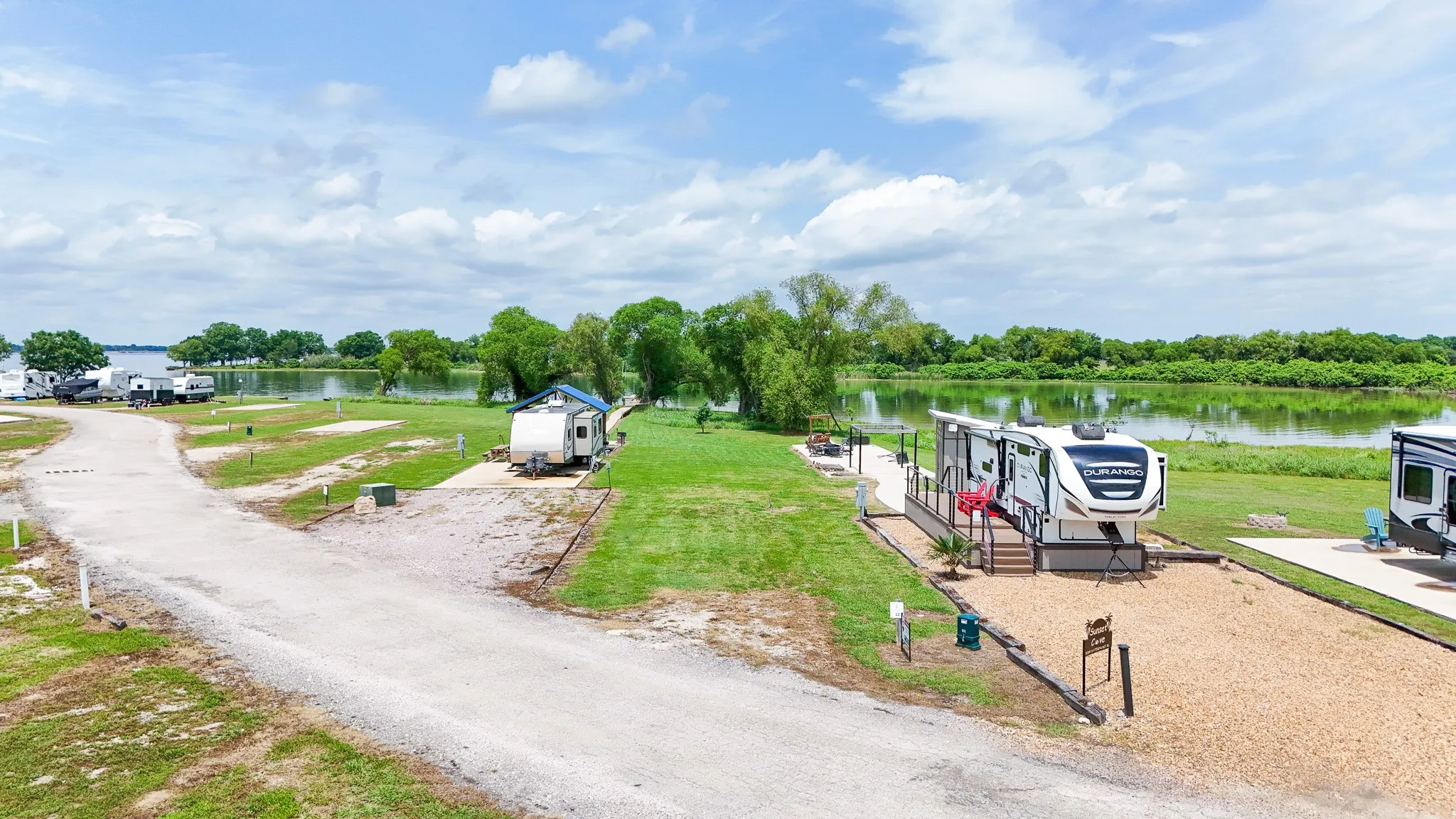 Waterfront RV lot featuring a gravel pad, an elevated deck, and a fire pit
