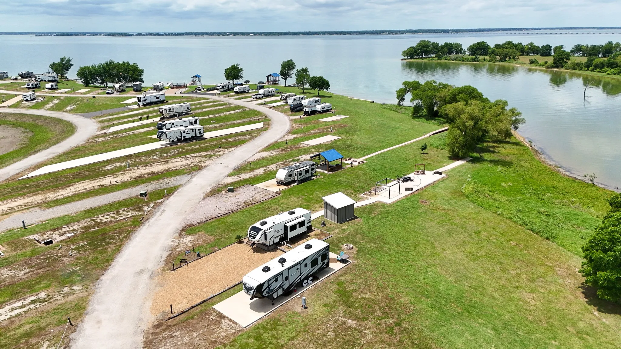 Waterfront property featuring multiple RV sites with gravel and concrete pads, established roadways, mature trees, and a covered pavilion