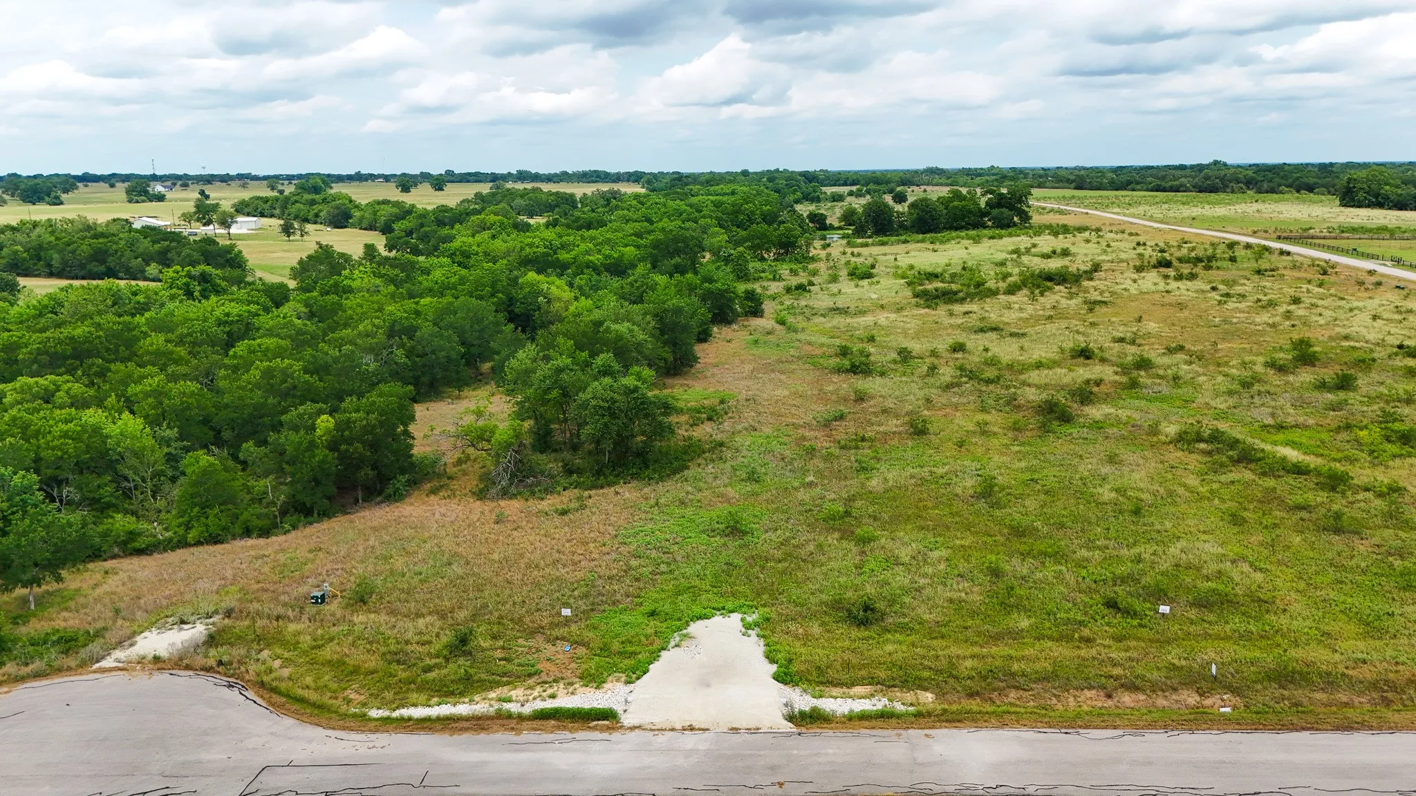 Expansive undeveloped land featuring a paved road frontage, mature tree lines, open grassy areas, and a partially graded entrance