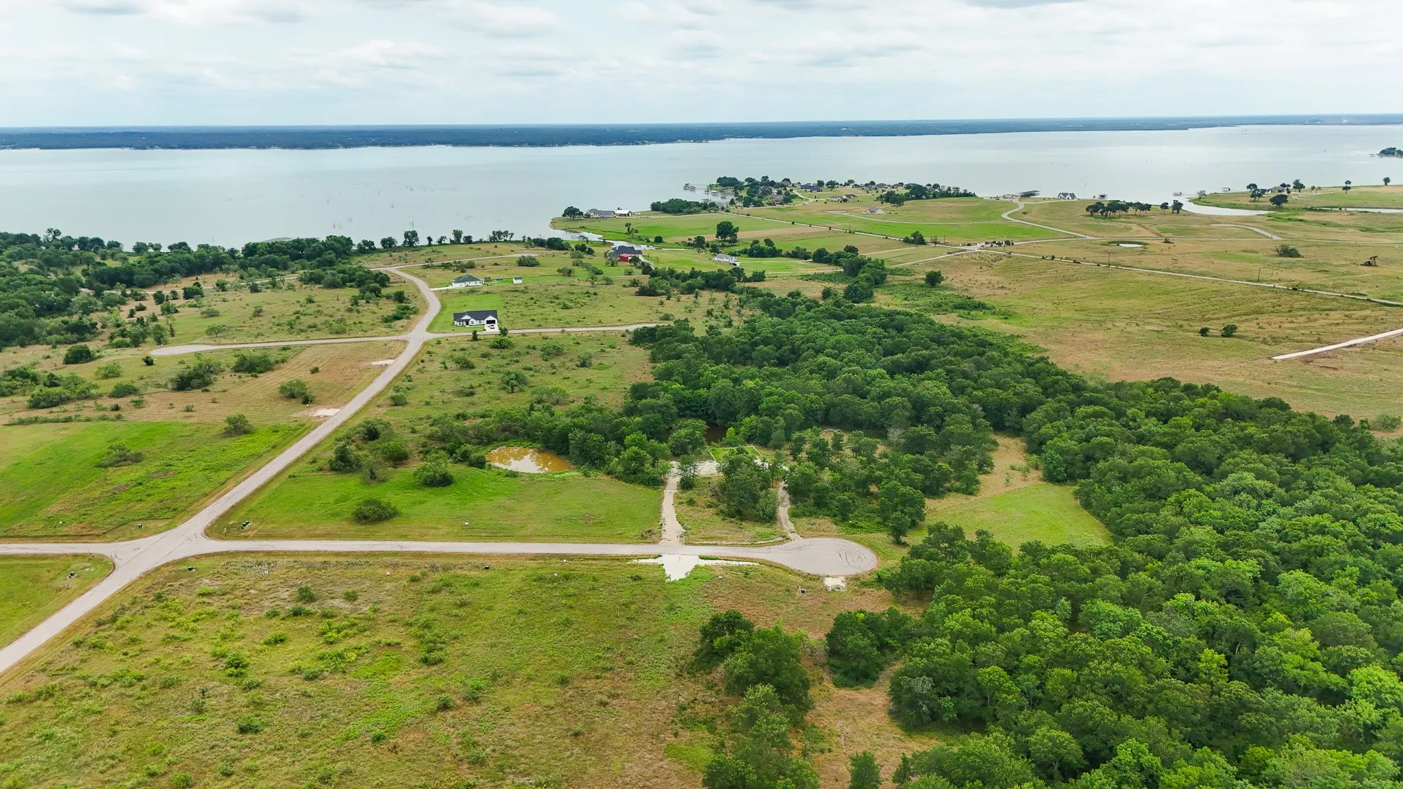 Expansive undeveloped land featuring a substantial tree line, cleared areas, a visible waterway, and paved road access
