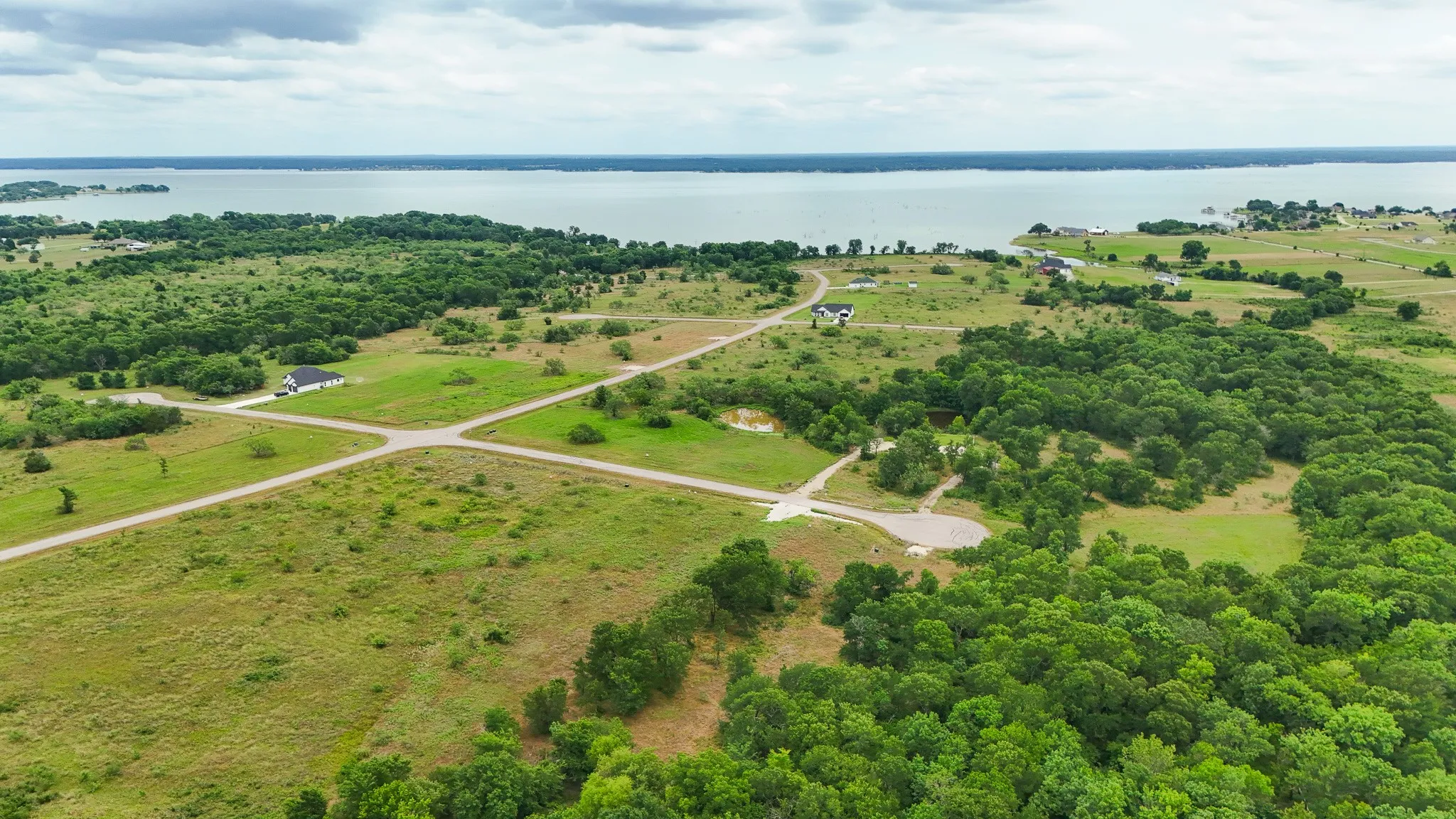 Expansive land parcel featuring partial tree coverage, established dirt roads, and distant water frontage