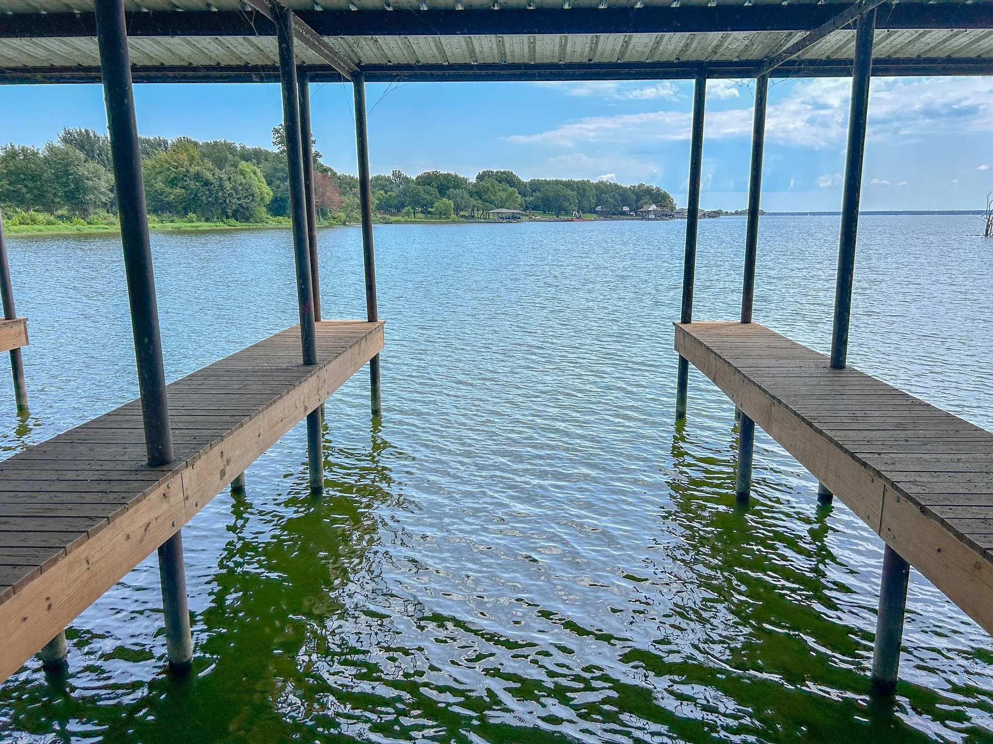 Covered boat dock featuring two slip openings with wood plank decking, metal support pilings, and a metal roof